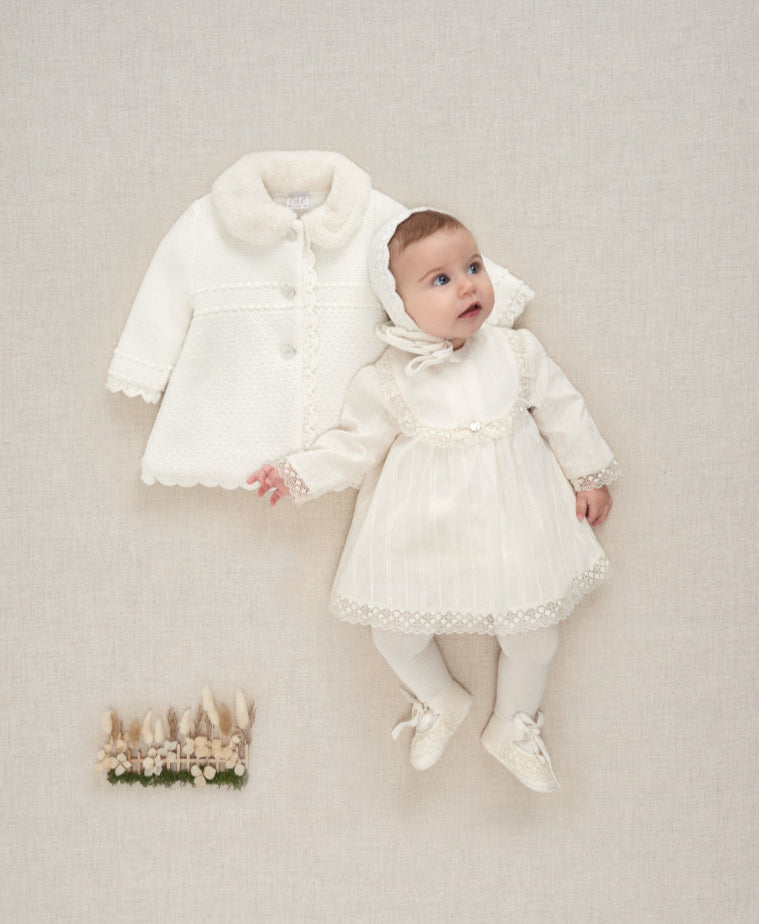 Baby in a white outfit with a fur-lined coat on a neutral background