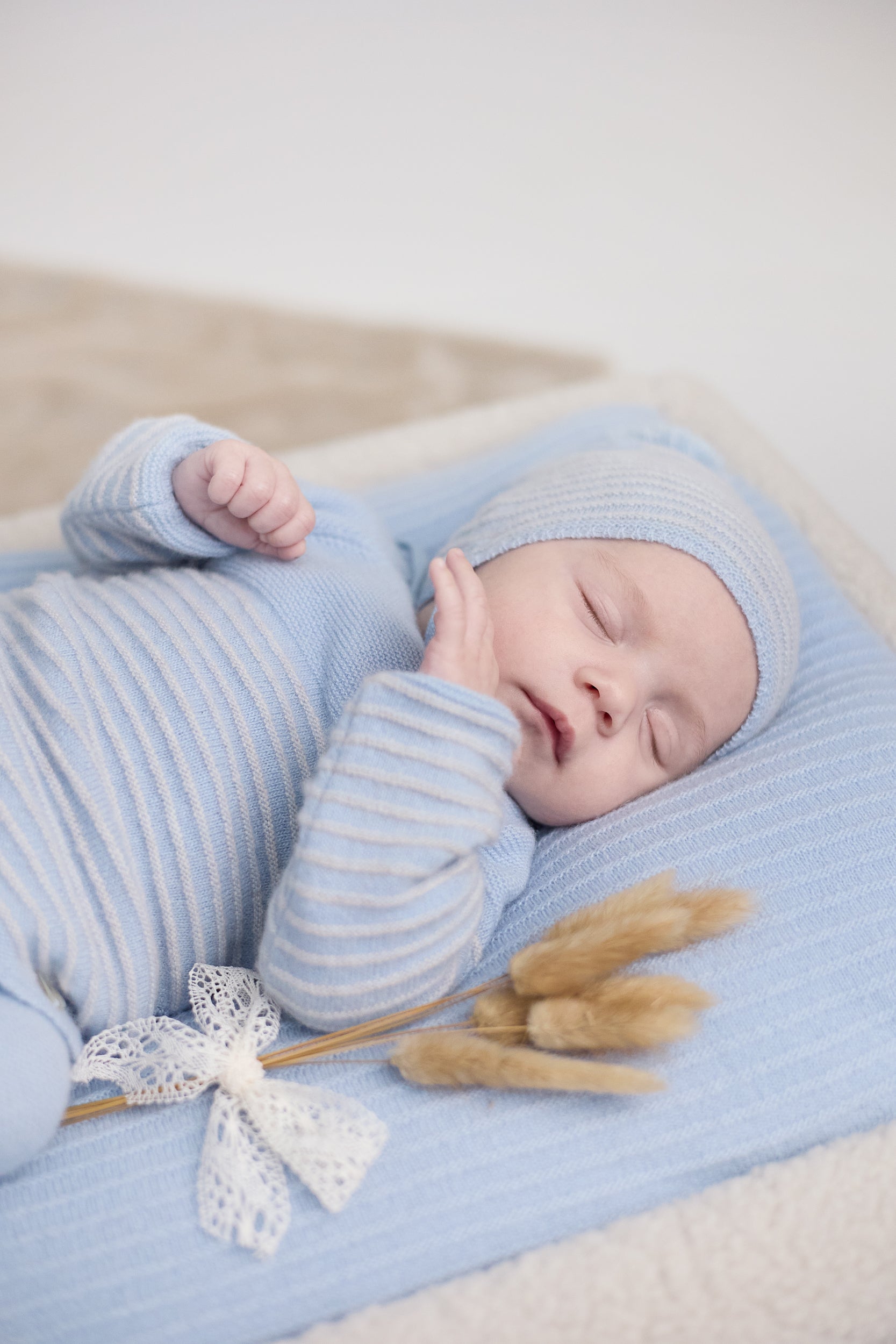 Newborn baby wrapped in blue stripes with a matching hat, lying on a blue blanket with decorative elements.
