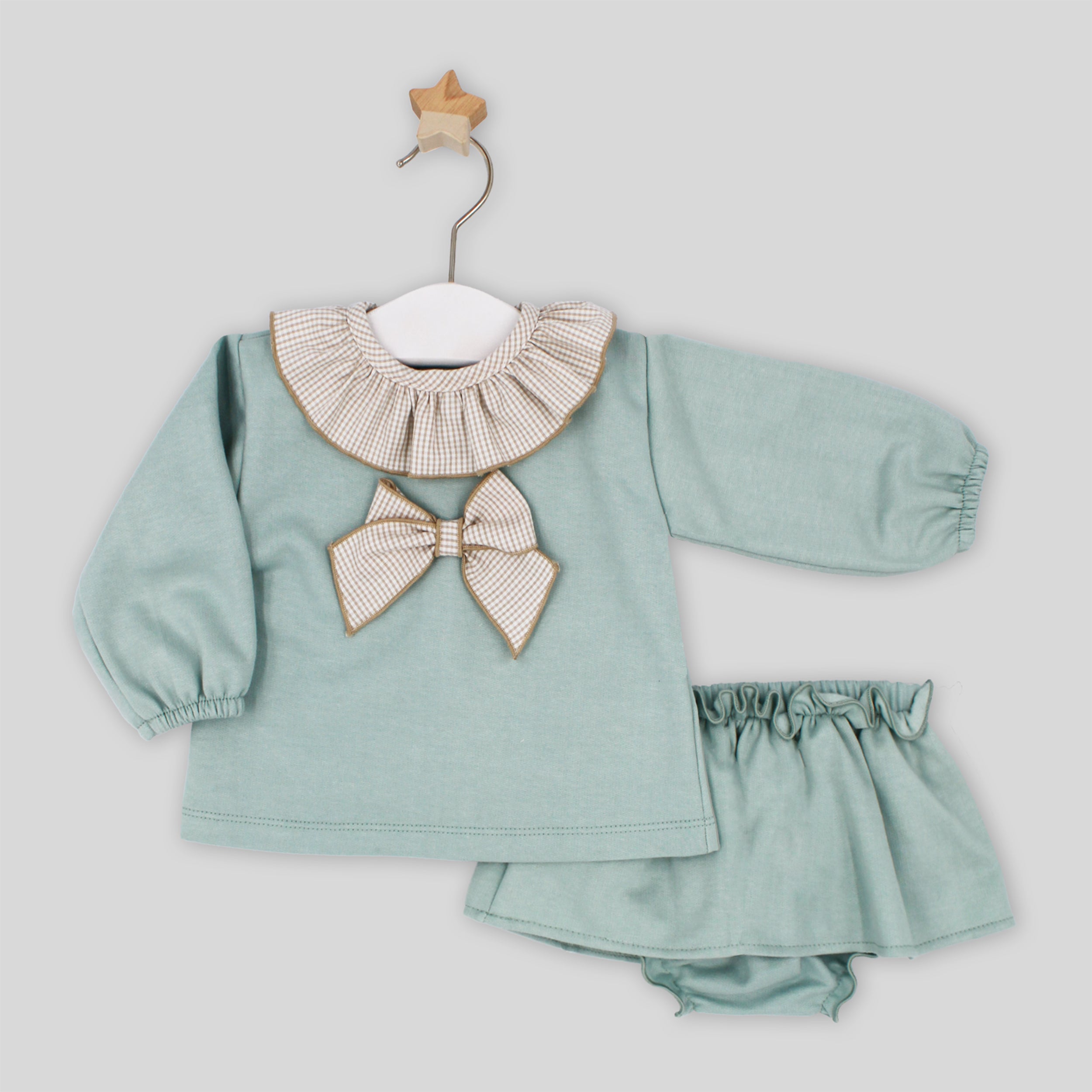 Children's outfit with green top and shorts on a hanger against a light gray background