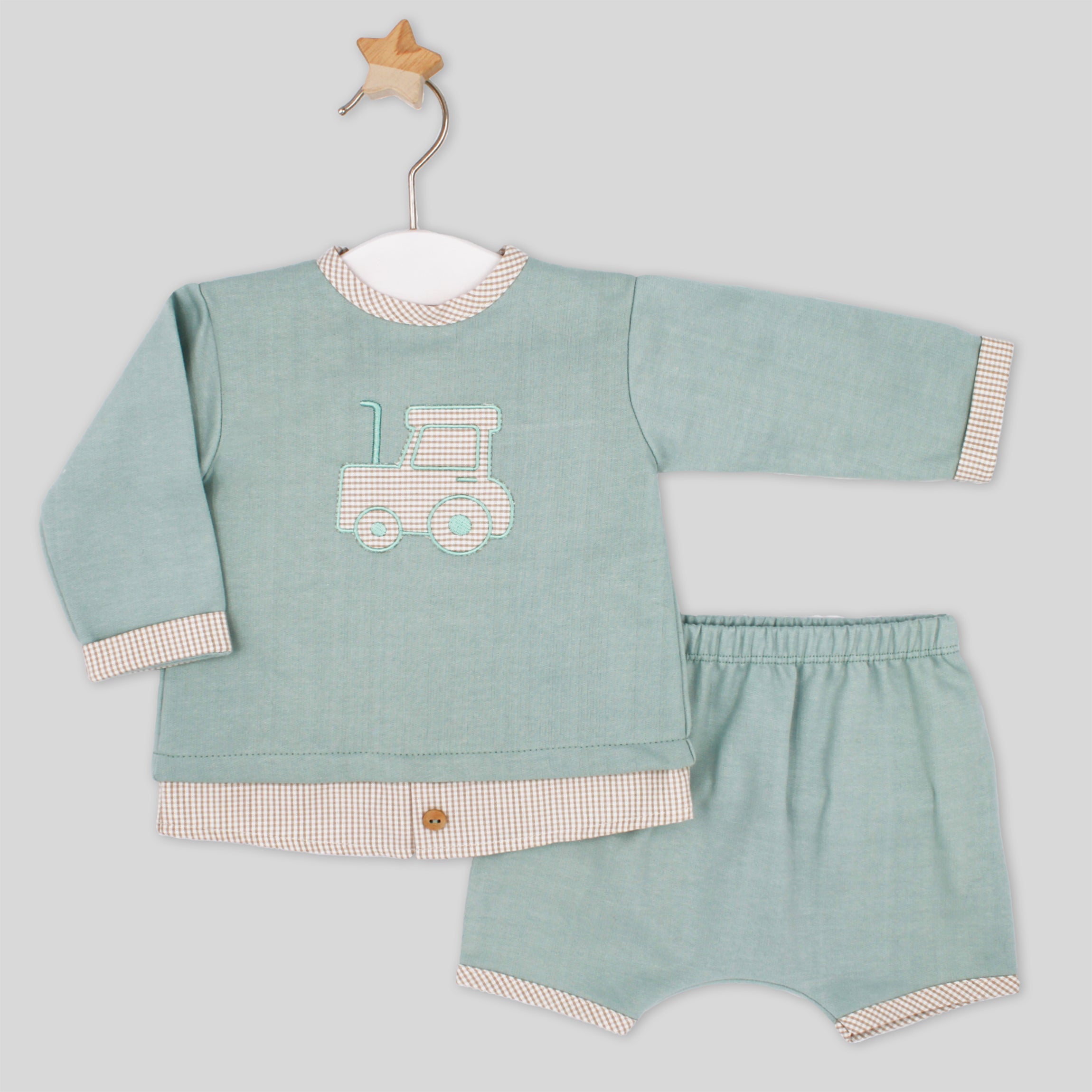 Children's outfit with a green shirt and shorts featuring a truck design on a light gray background.
