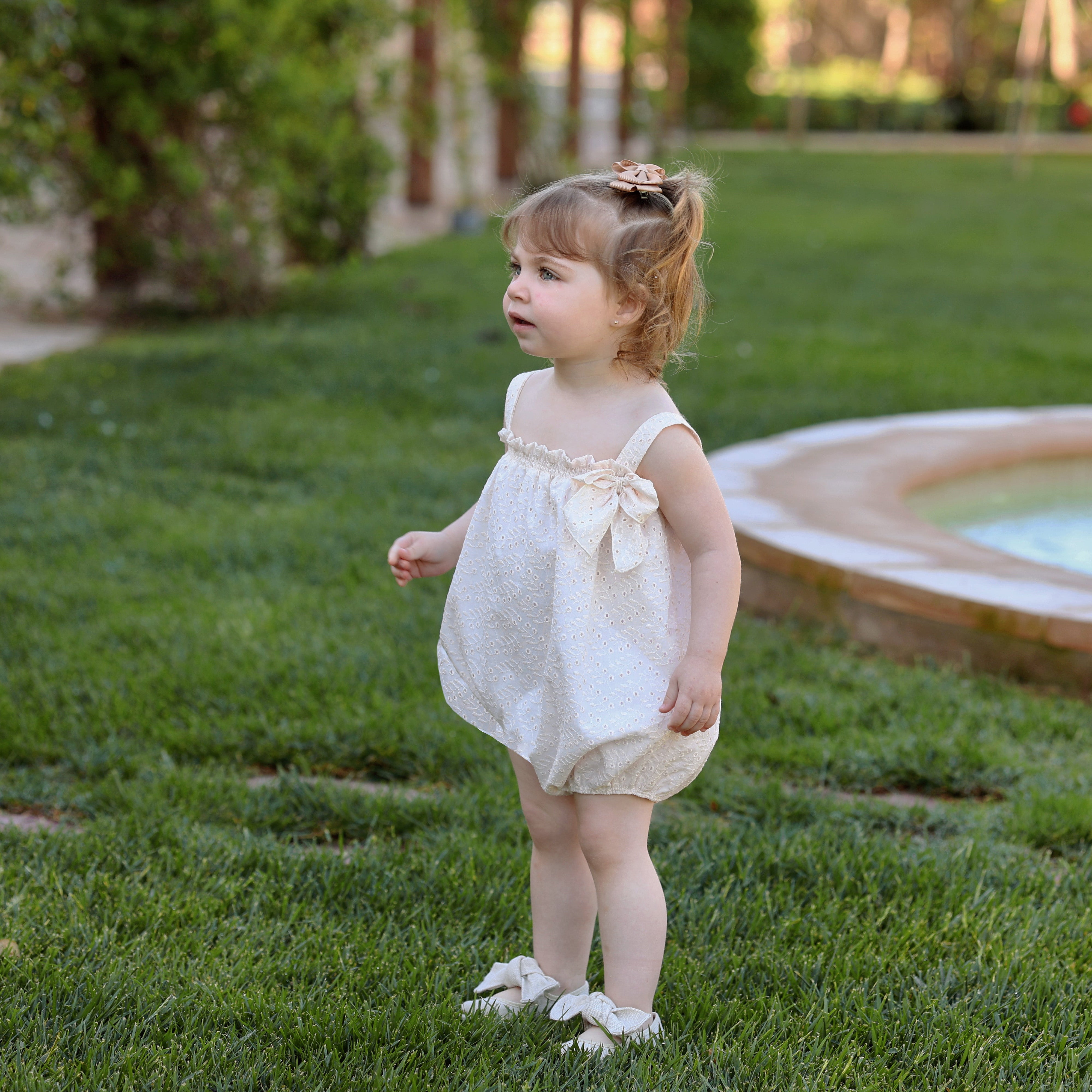 Young girl in a white dress standing on grass near a pool