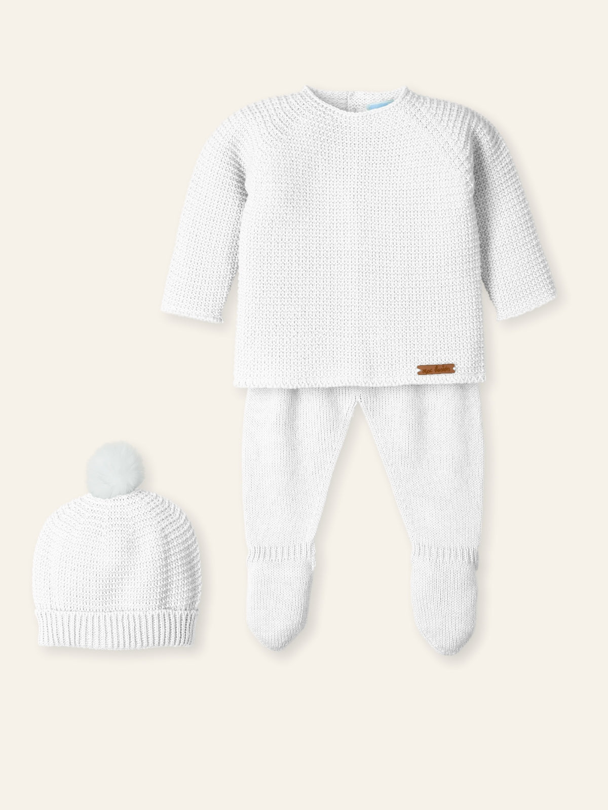Baby outfit with white sweater, pants, and hat on a beige background