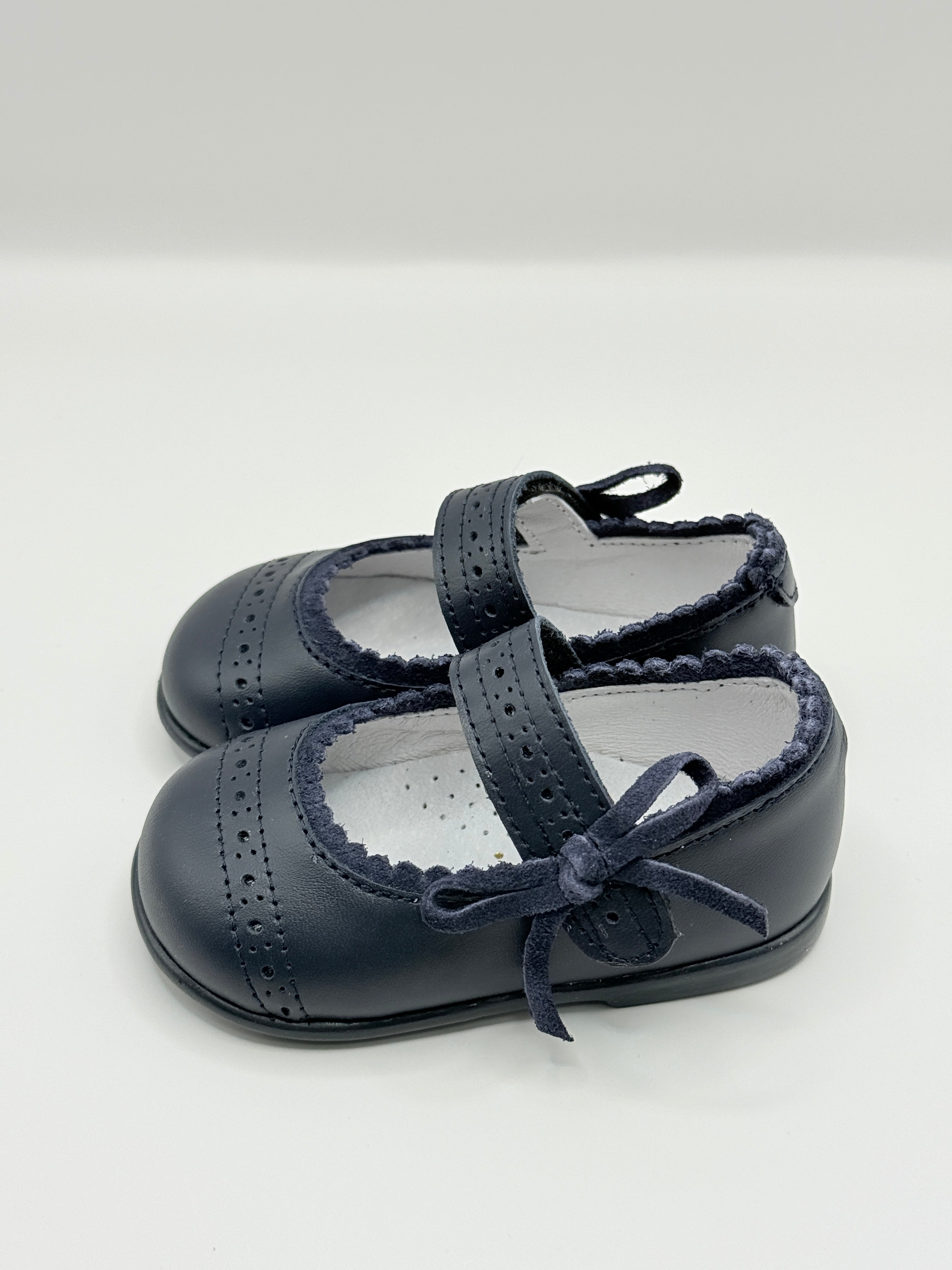 Pair of navy blue children's shoes with bow details on a light gray background