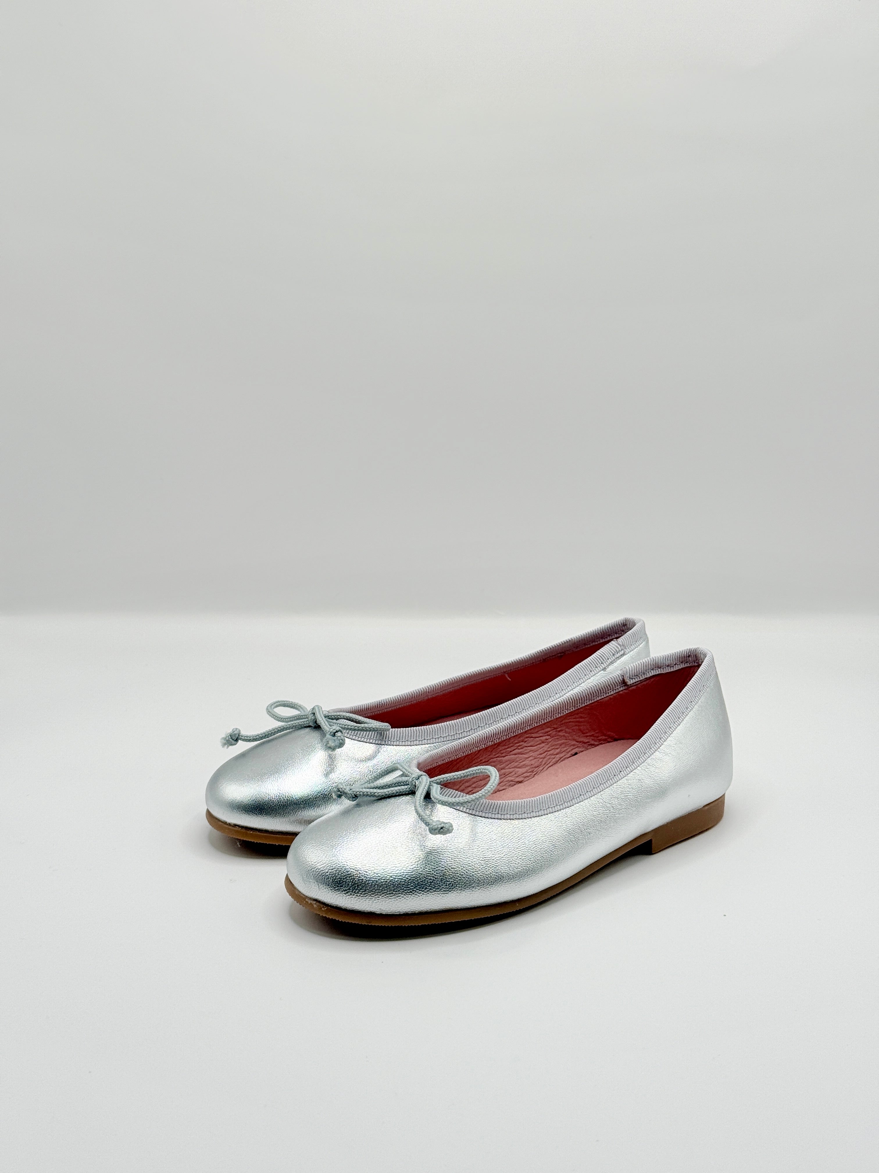 Pair of silver shoes with a bow on a light gray background