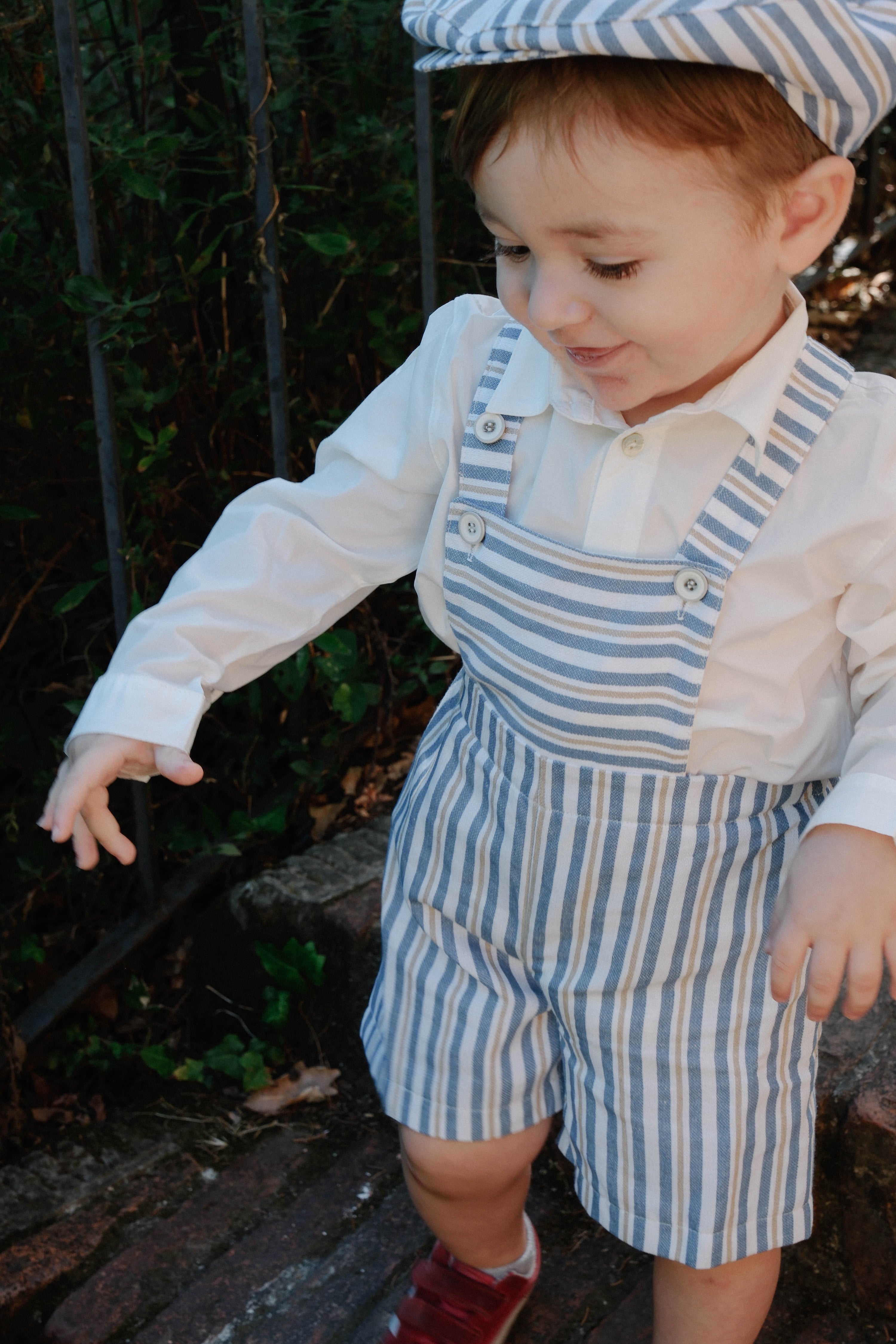 Child wearing a blue and white striped outfit with a matching hat outdoors.