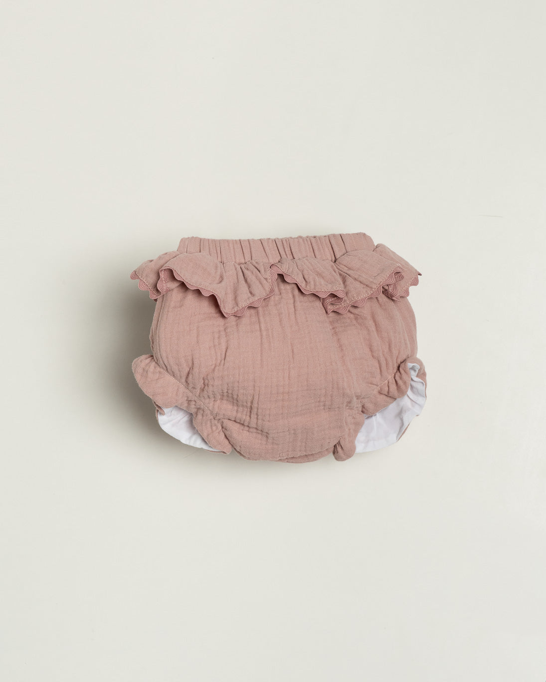 Pink baby bloomers with ruffles on a beige background
