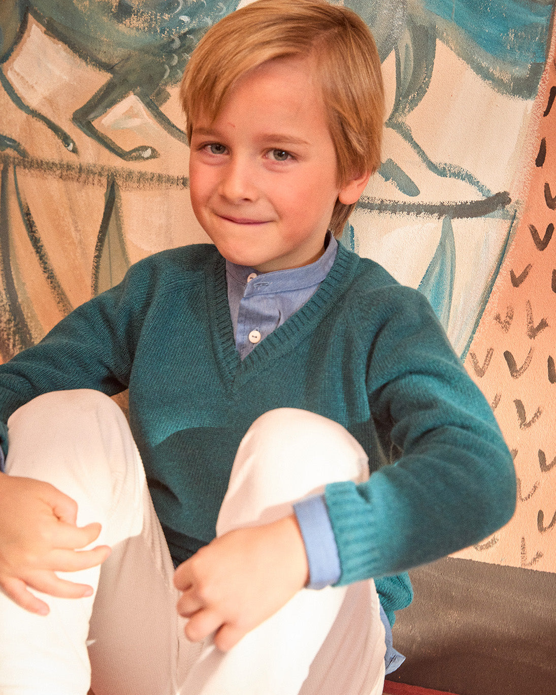 Young boy wearing a teal sweater with a patterned wall in the background