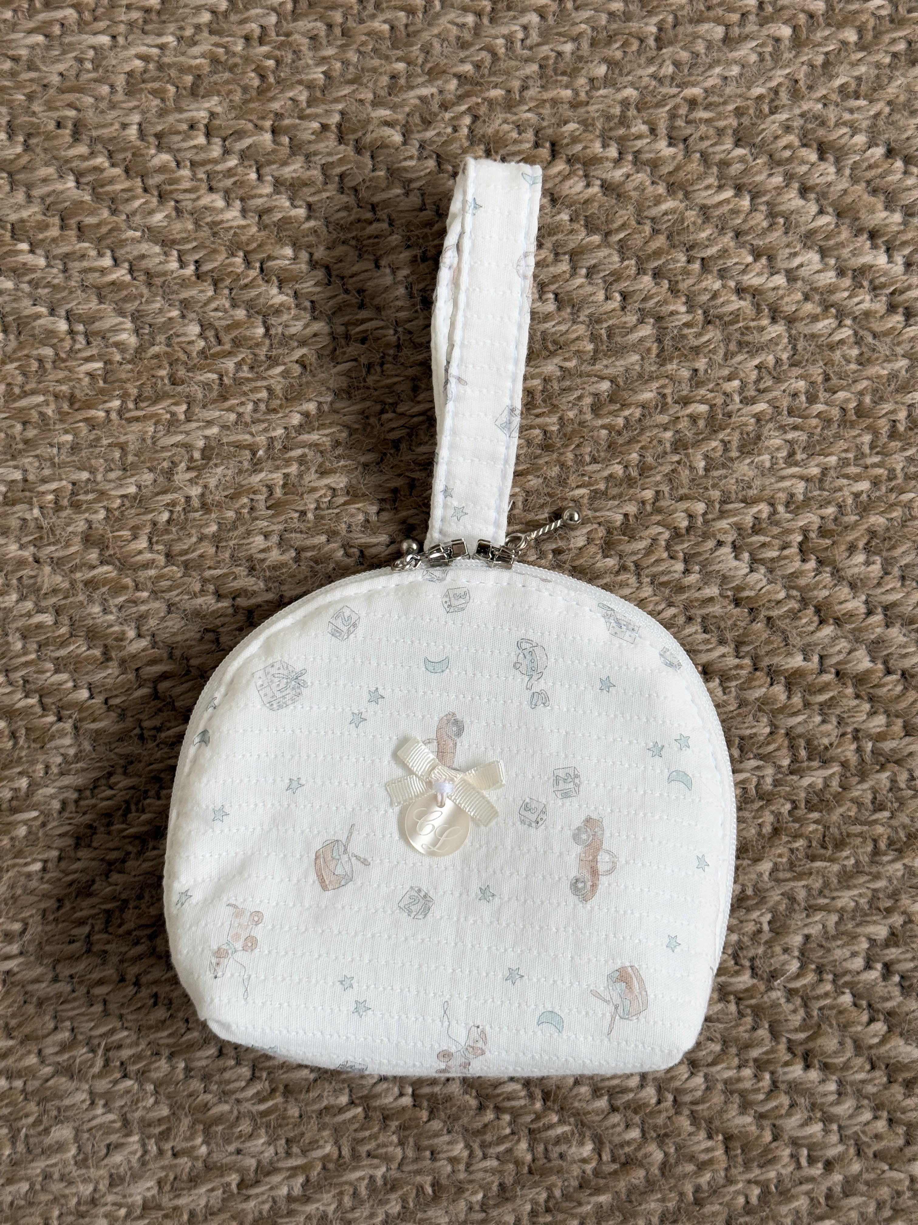 Small round white fabric pouch with a floral pattern on a brown textured background