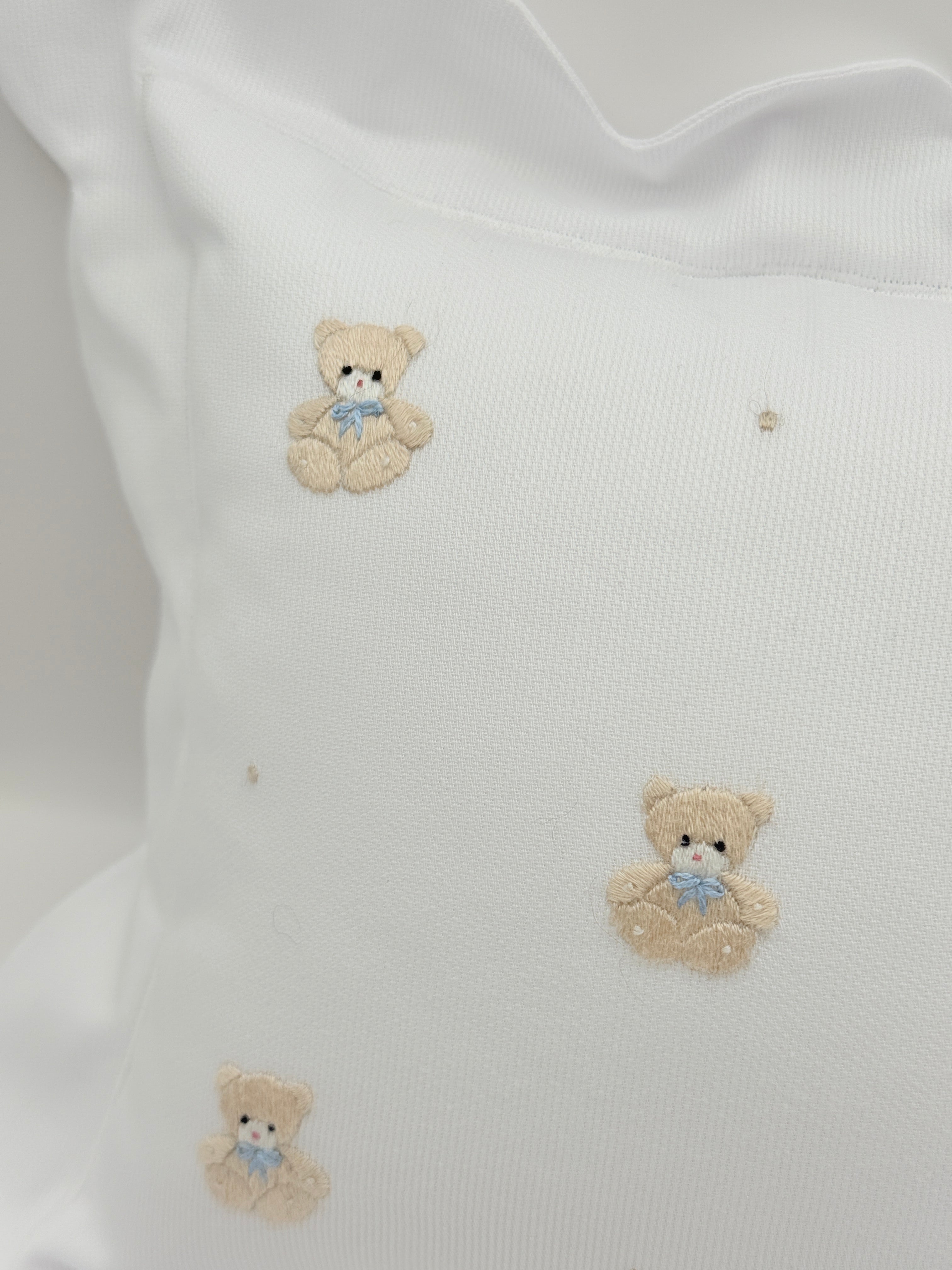White fabric with embroidered teddy bear designs on a light grey background