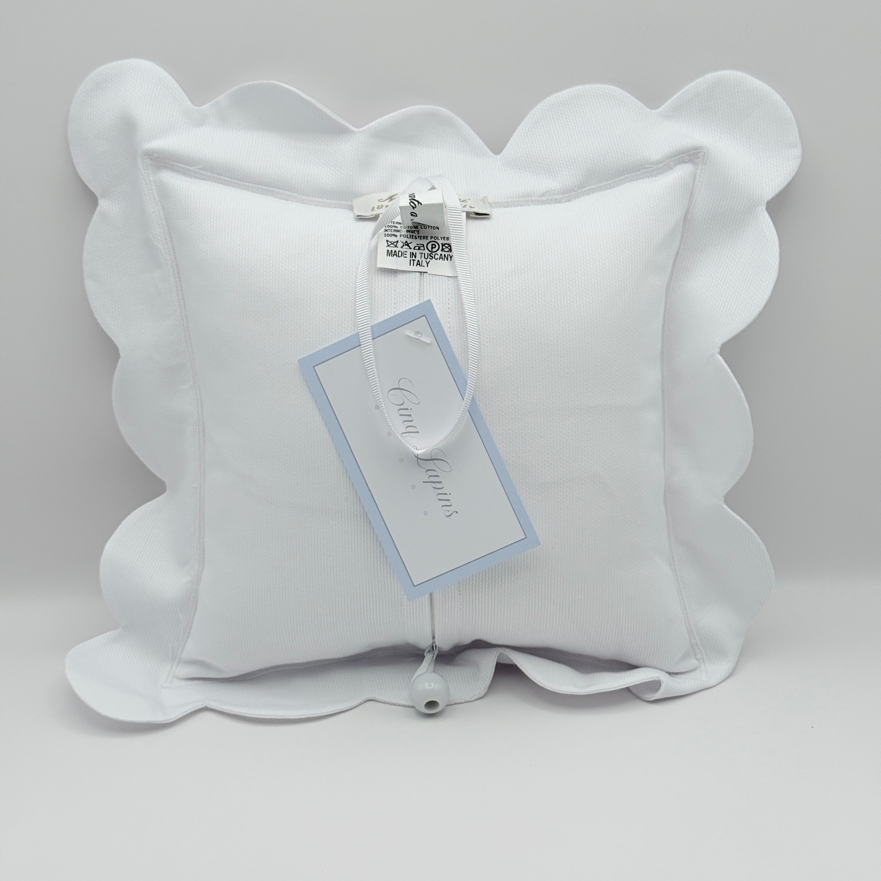 White scalloped ring pillow with a tag on a light gray background