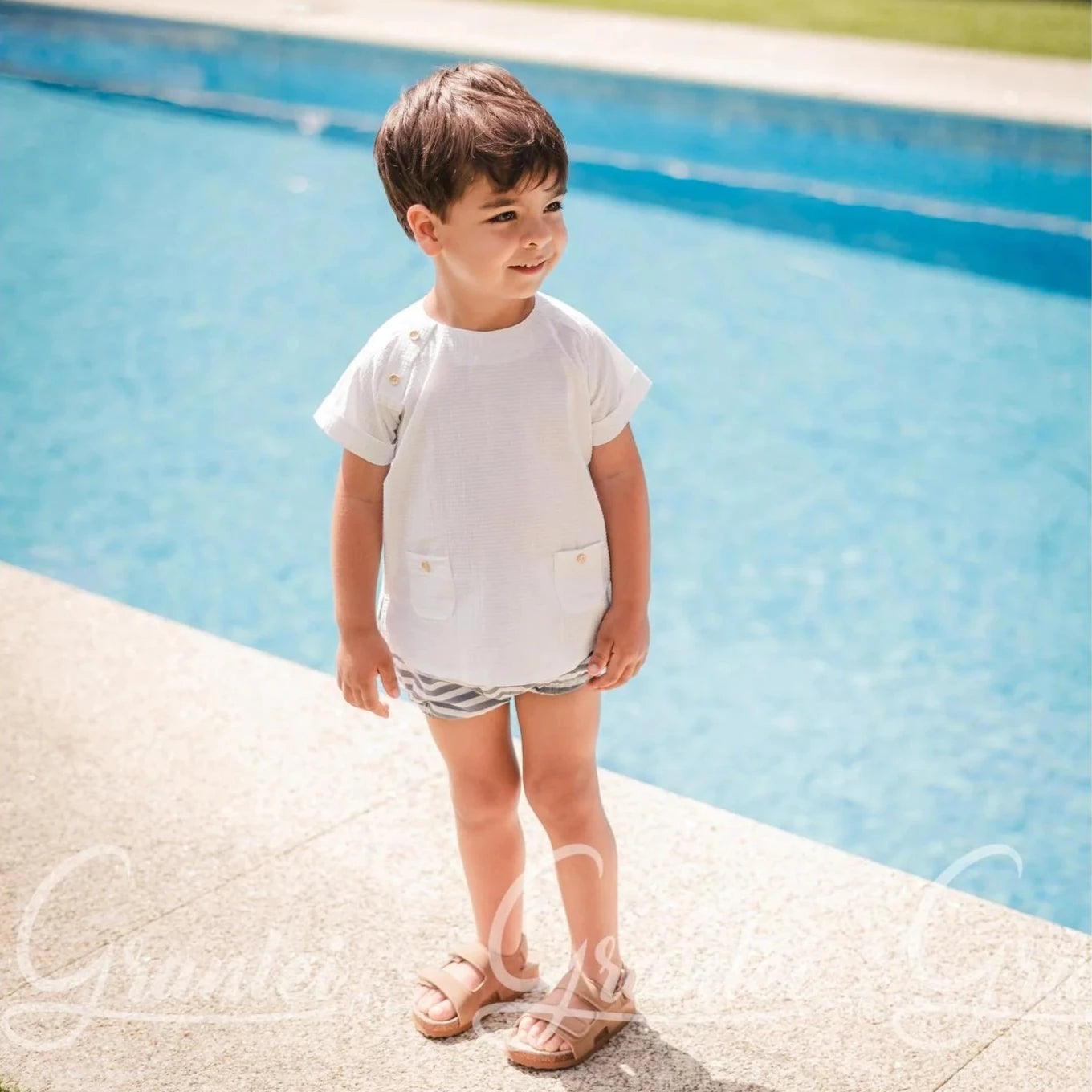Child standing by a pool with a stone wall and grass in the background