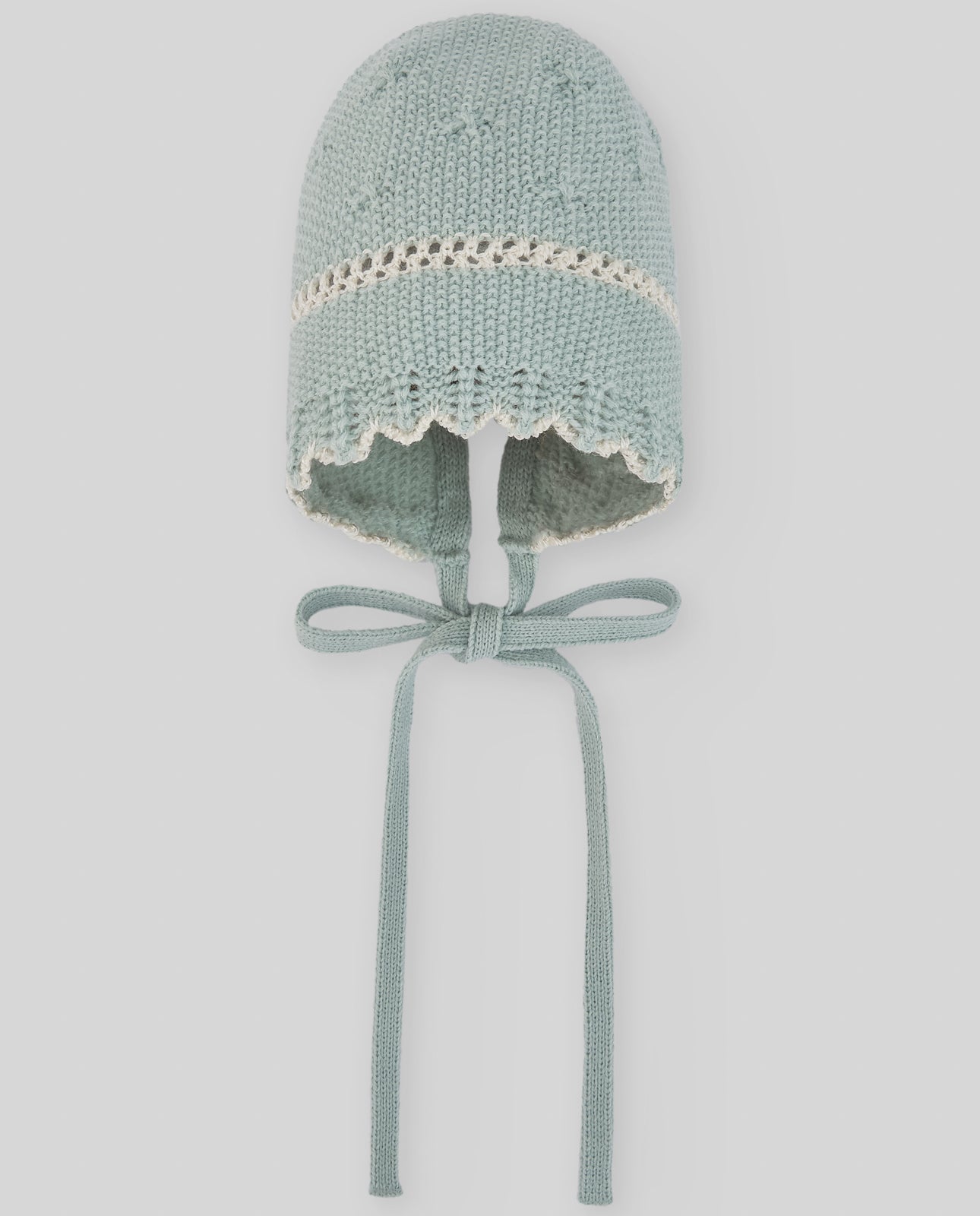 Knitted baby bonnet with lace trim on a light gray background