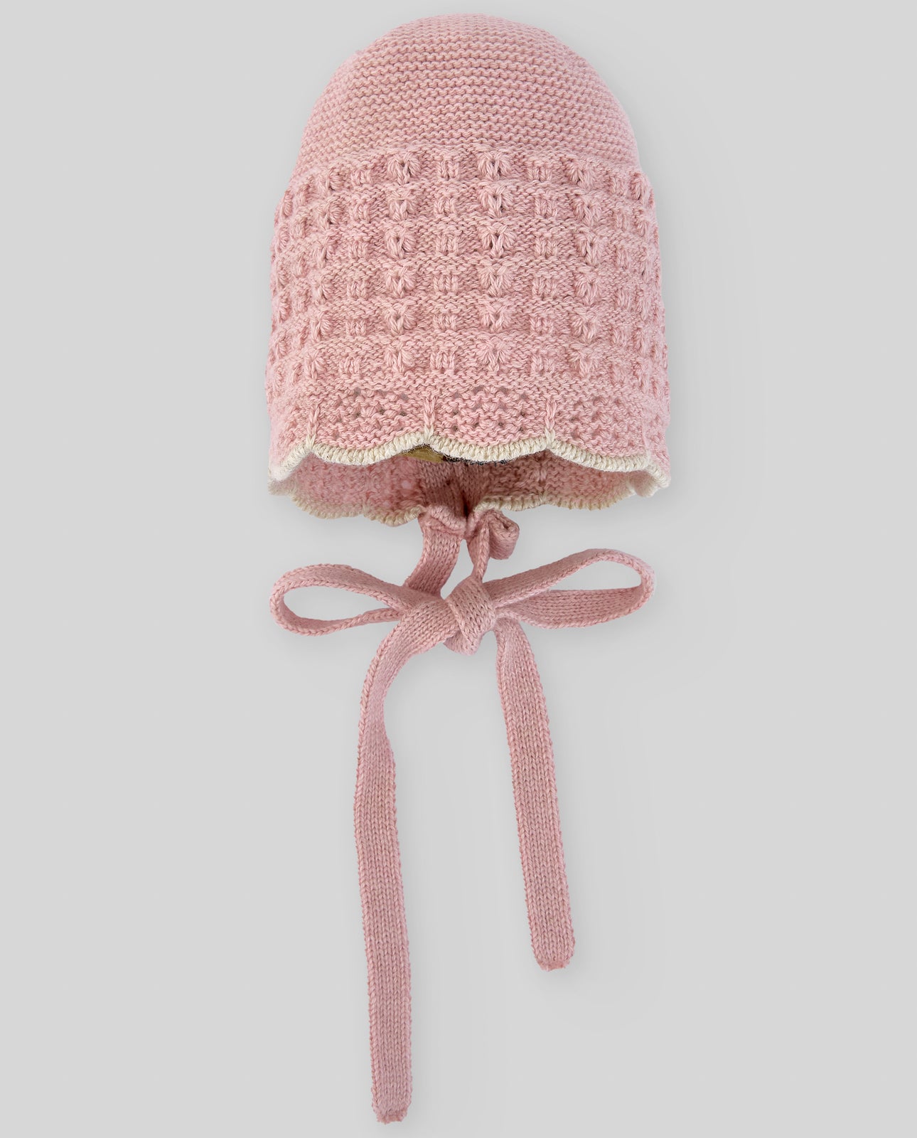 Pink knitted baby bonnet with a bow on a light gray background