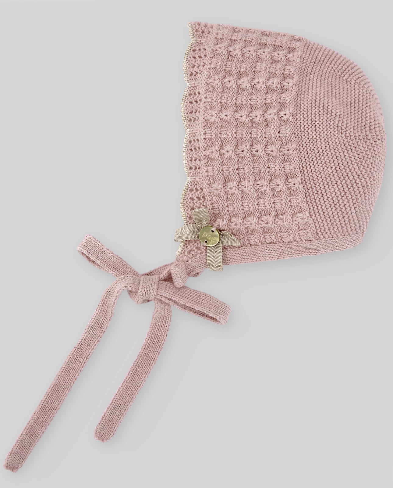 Pink knitted baby bonnet with a bow on a light gray background