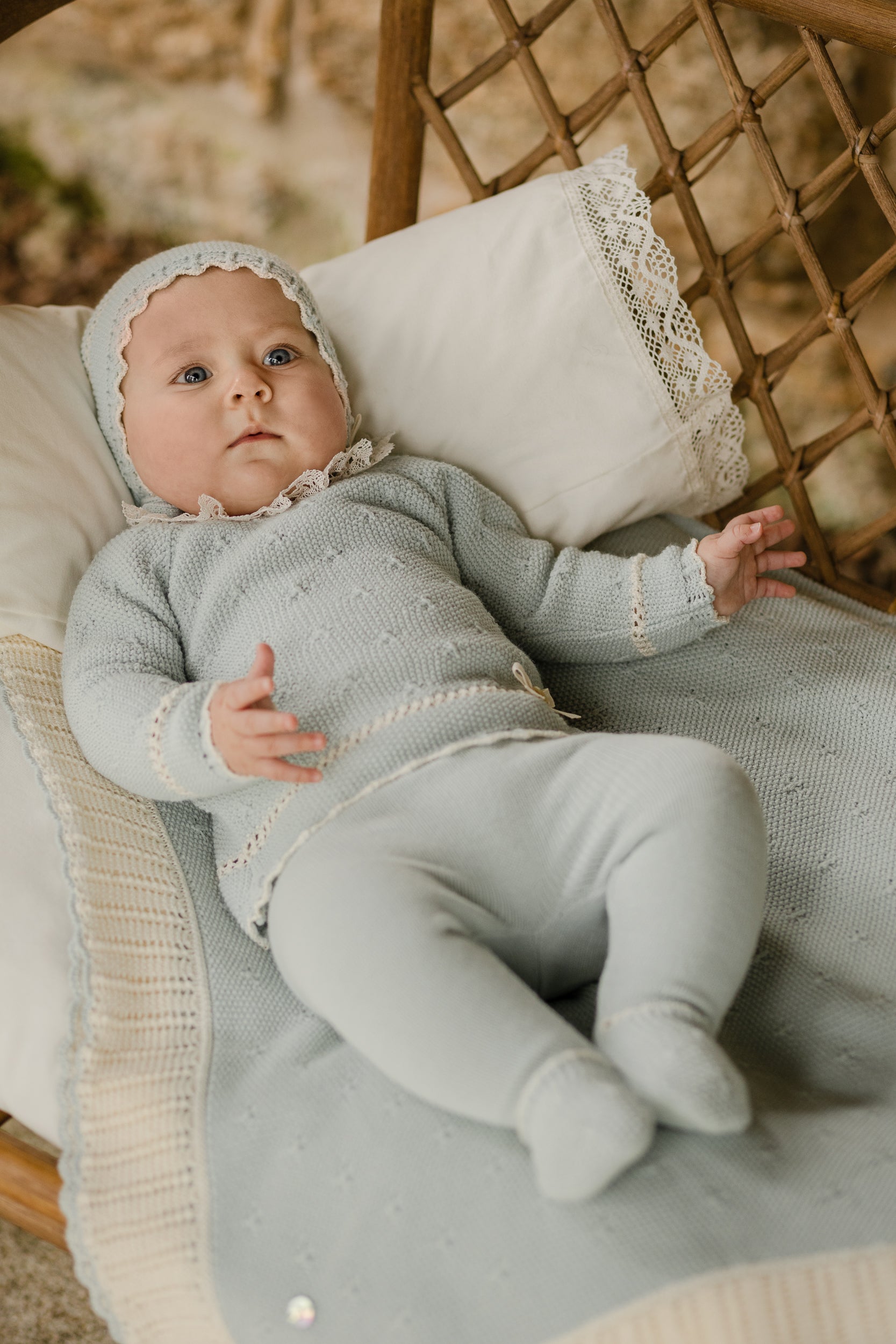 Baby in a light green outfit sitting on a wicker chair with a textured cushion.
