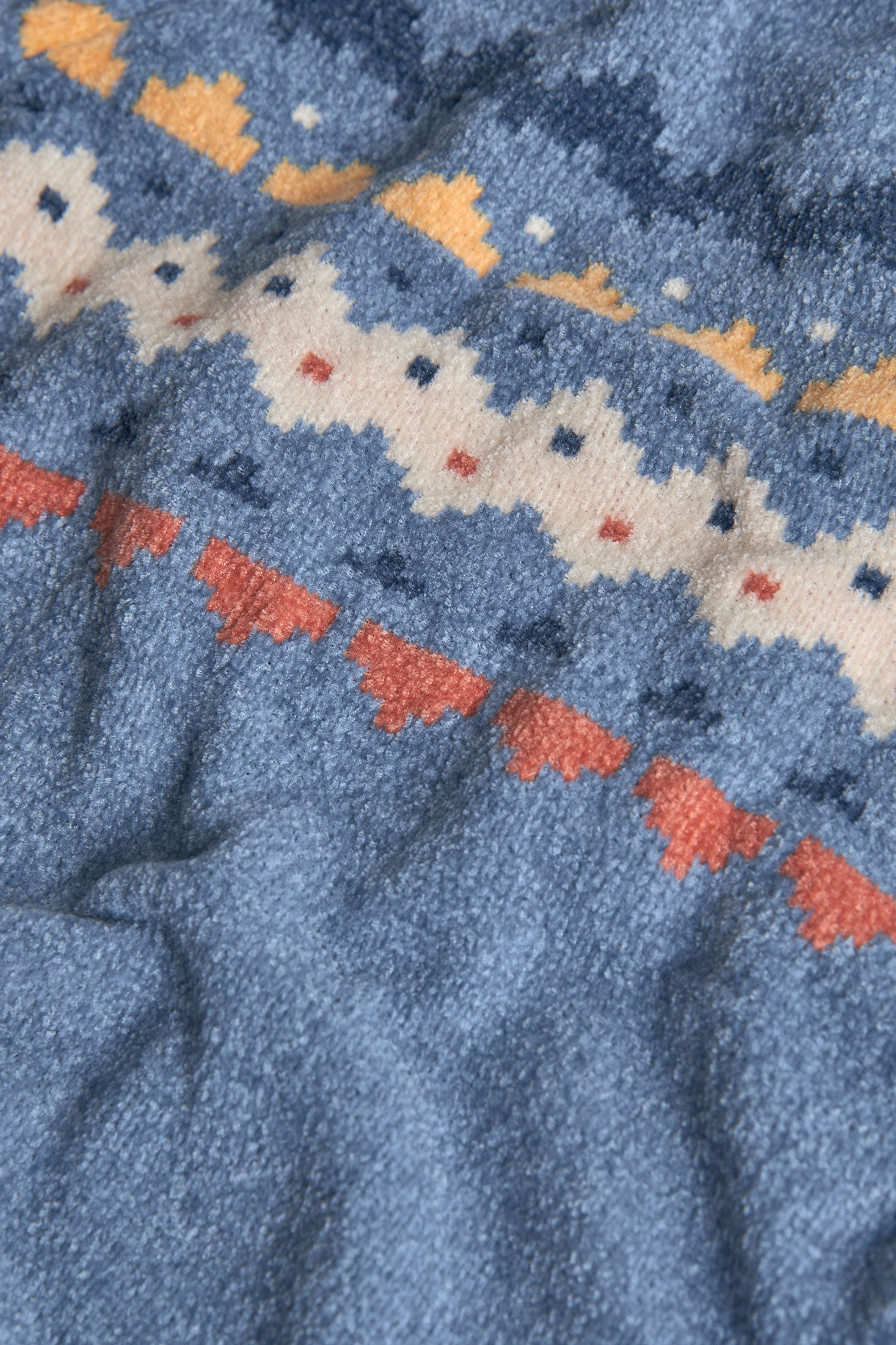 Close-up of a blue fabric with a patterned border featuring orange, white, and red colors.