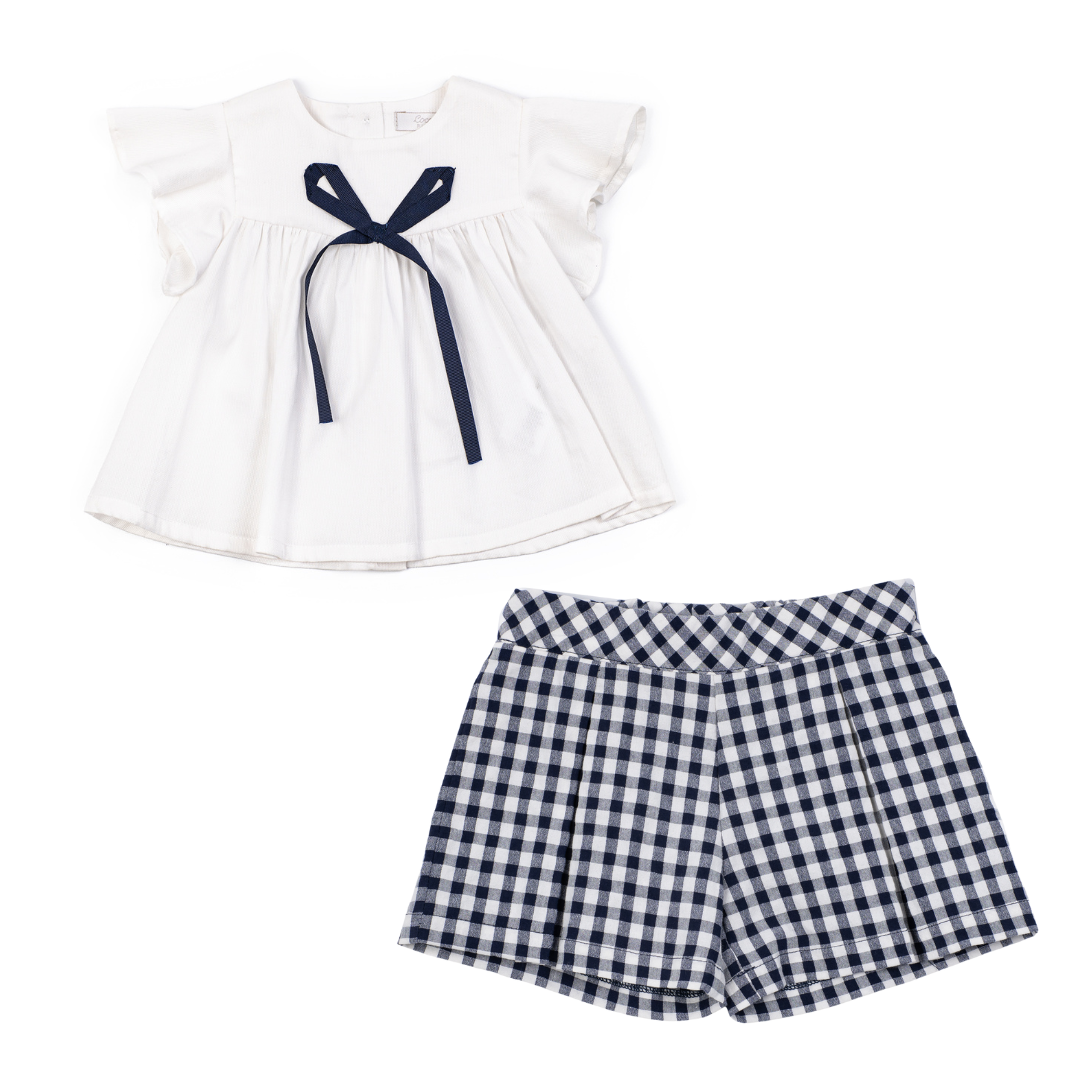 White blouse with navy bow and checkered shorts on a white background