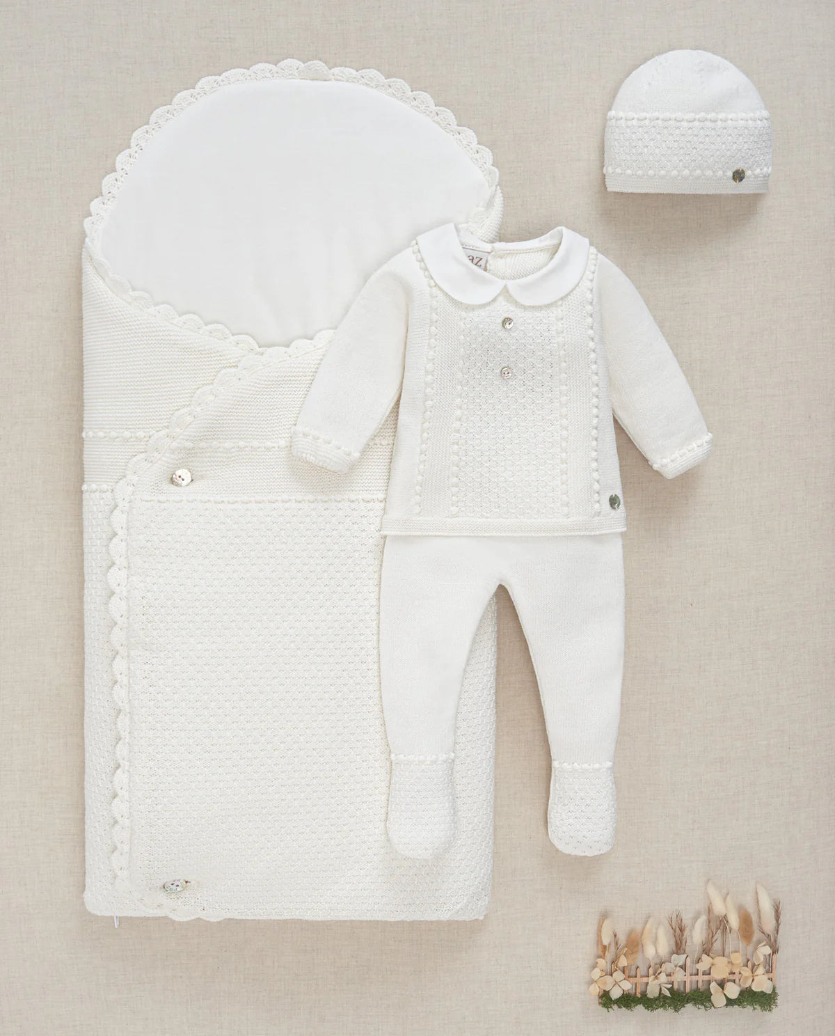 White baby outfit with hat and blanket on a beige background