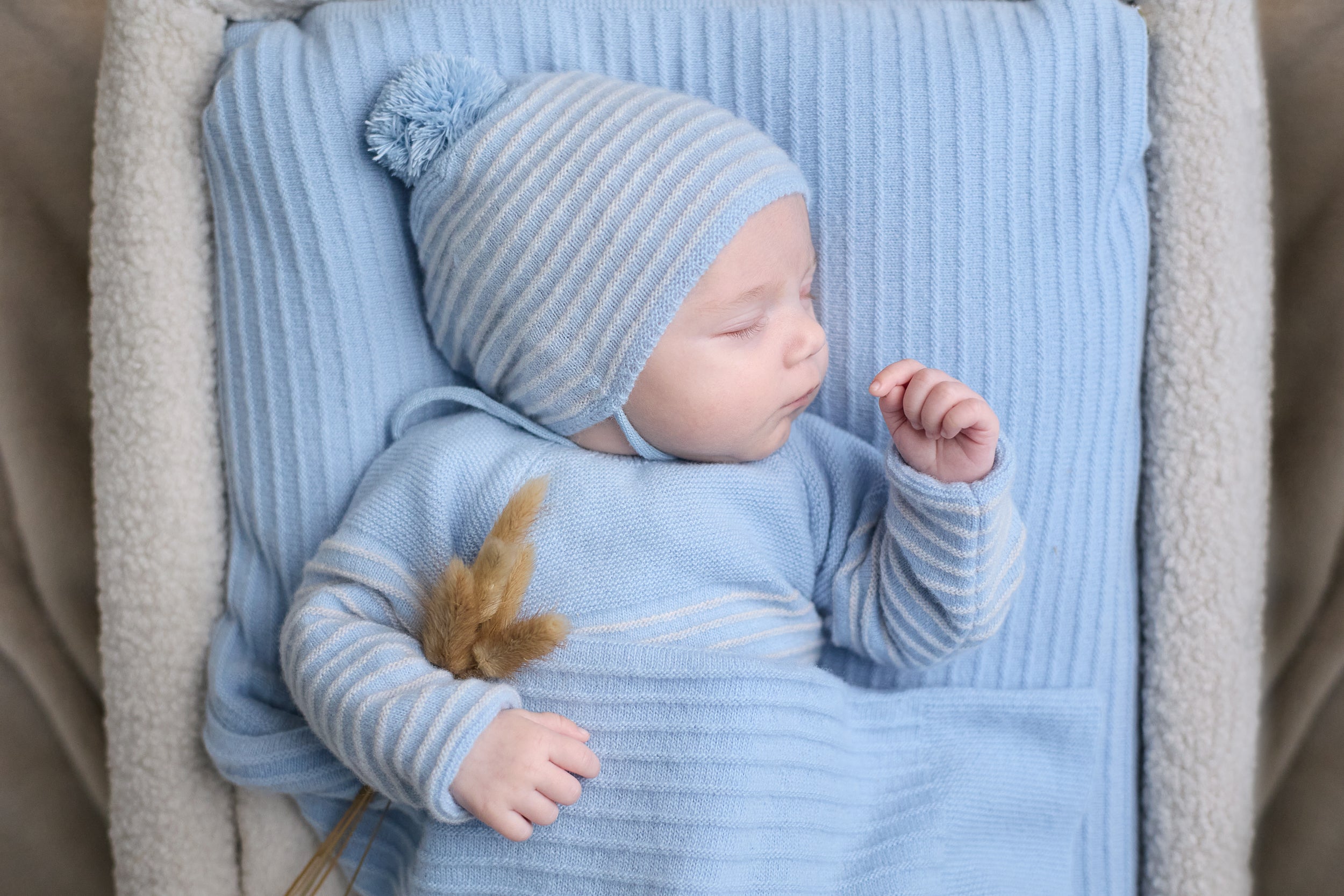 Newborn baby in blue outfit and hat sleeping on a textured blanket