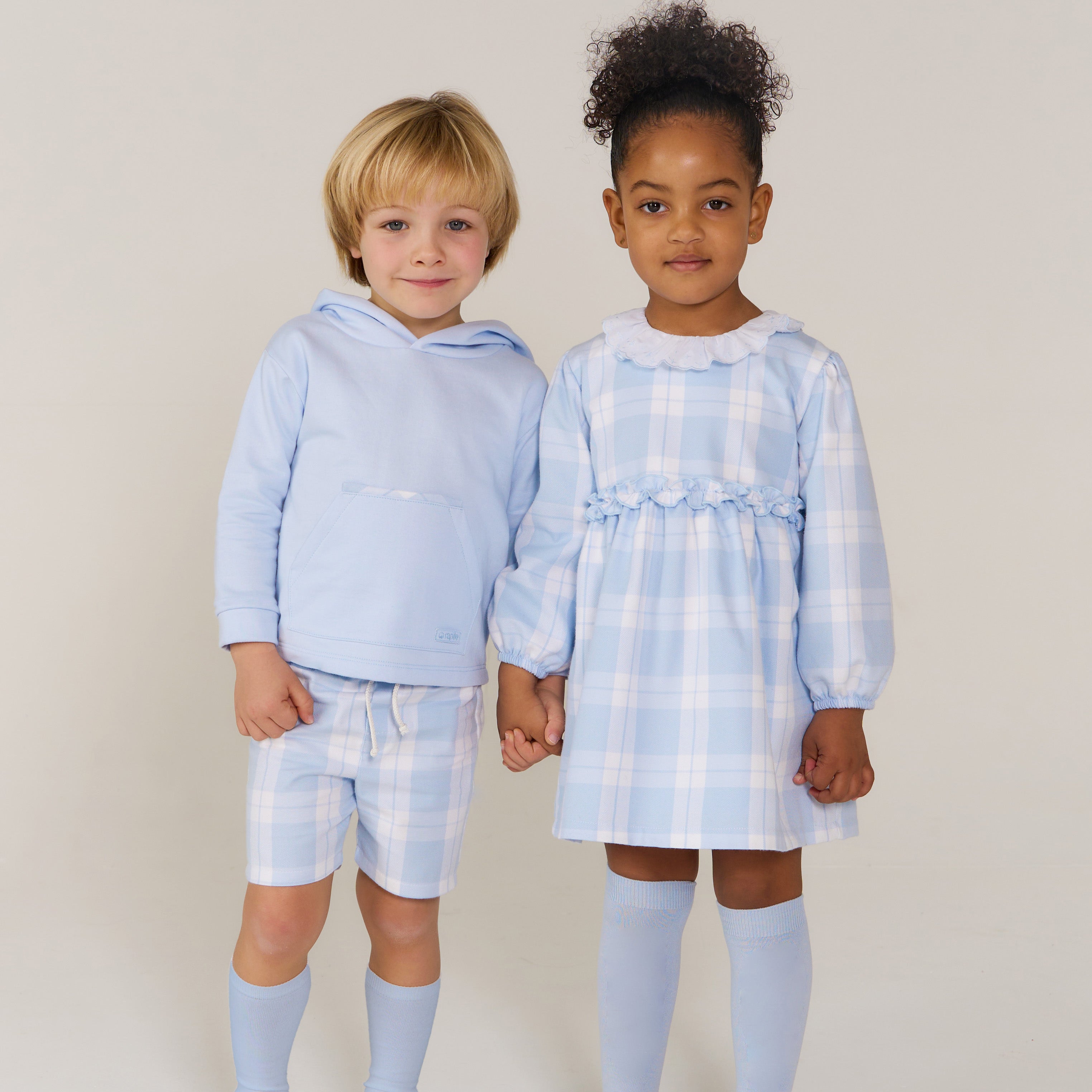 Two children wearing matching blue checkered outfits against a plain background