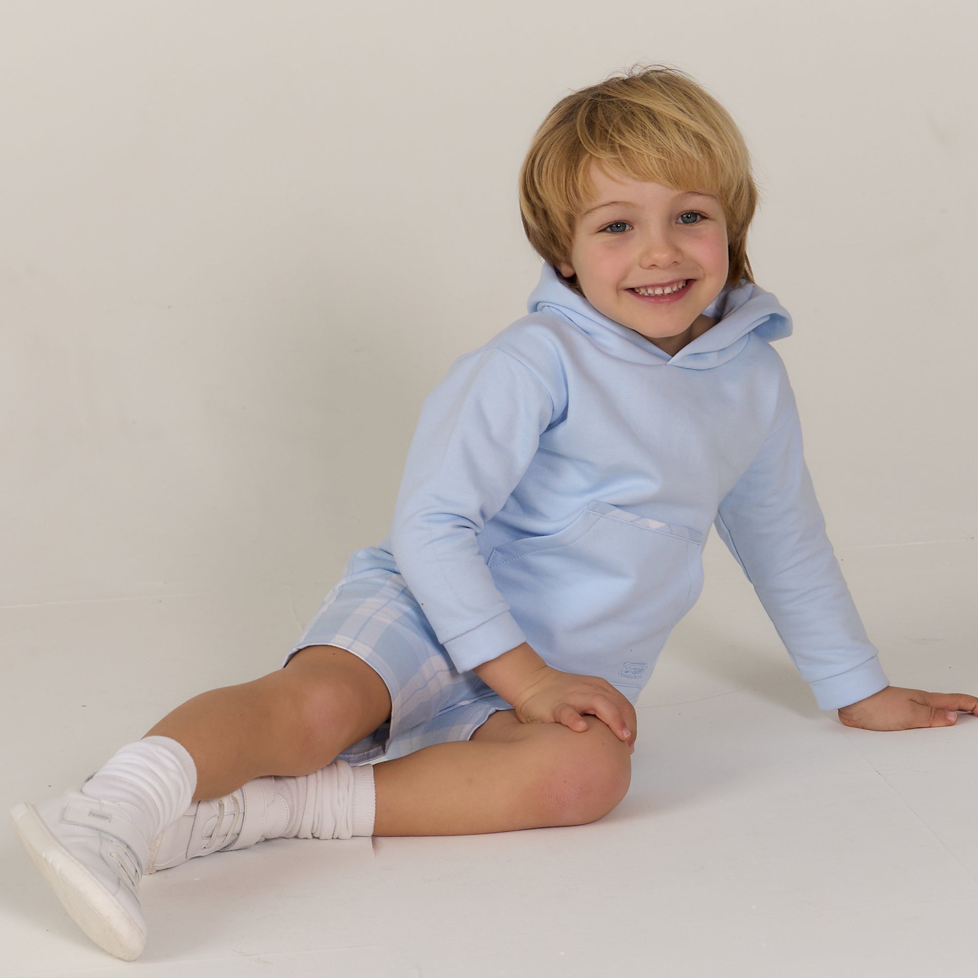 Child wearing a light blue hoodie and shorts sitting on a white surface.
