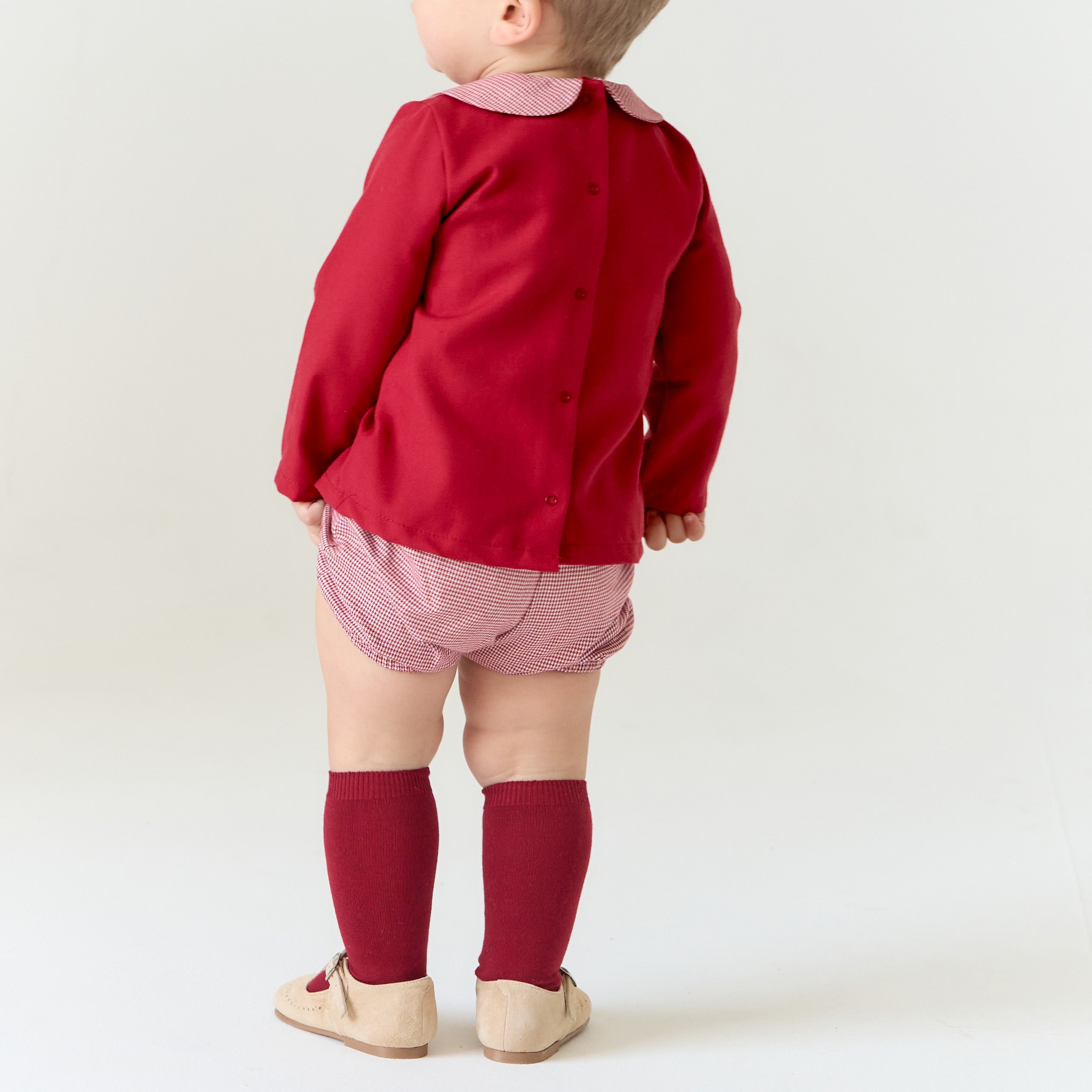 Child wearing a red shirt, pink shorts, and red socks on a white background