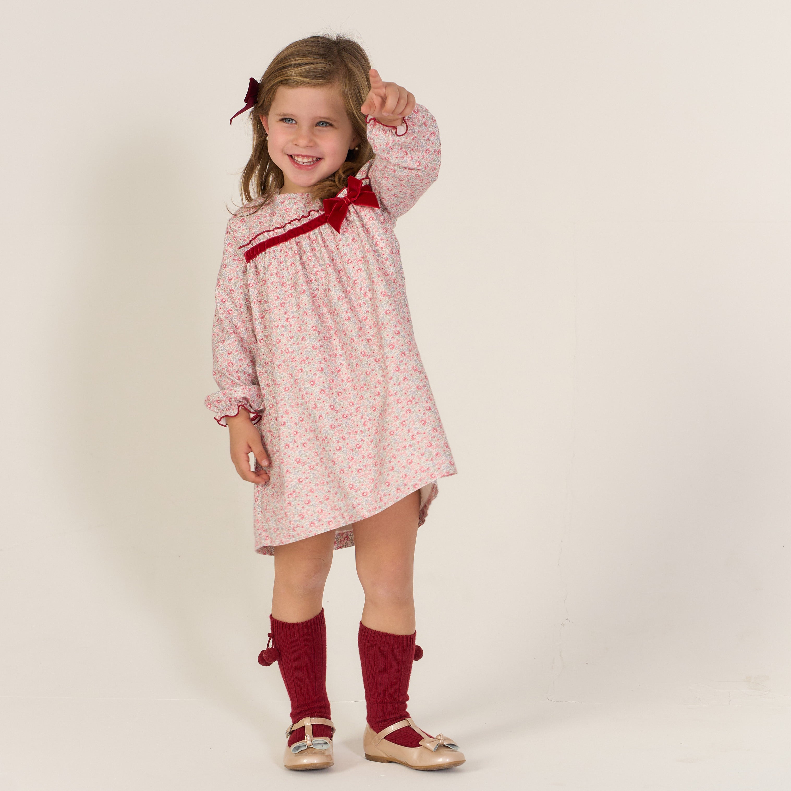 Young girl wearing a pink floral dress with a red bow and red knee-high socks on a white background