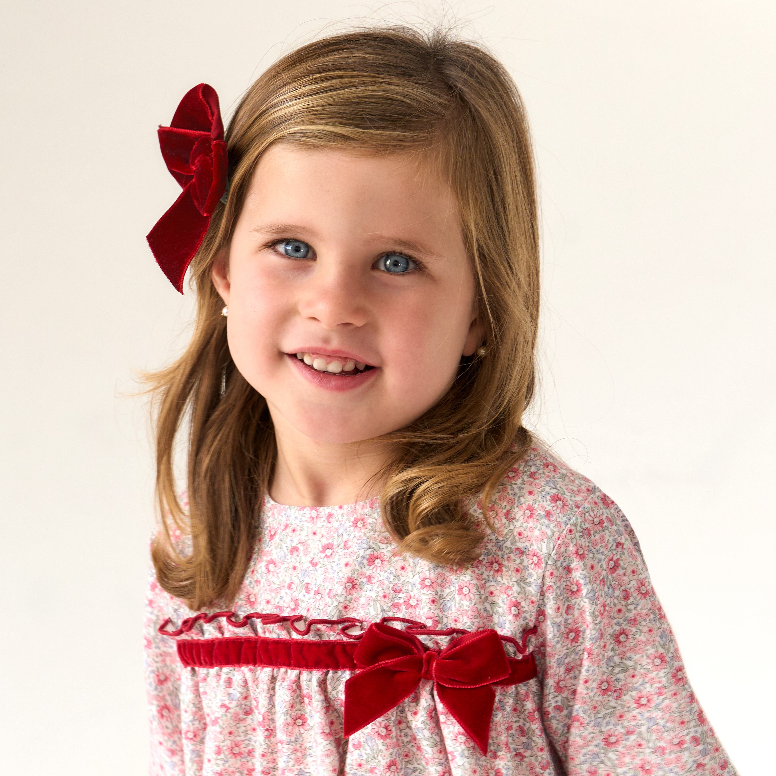 Young girl wearing a floral dress with red accents and a red hair bow against a plain background