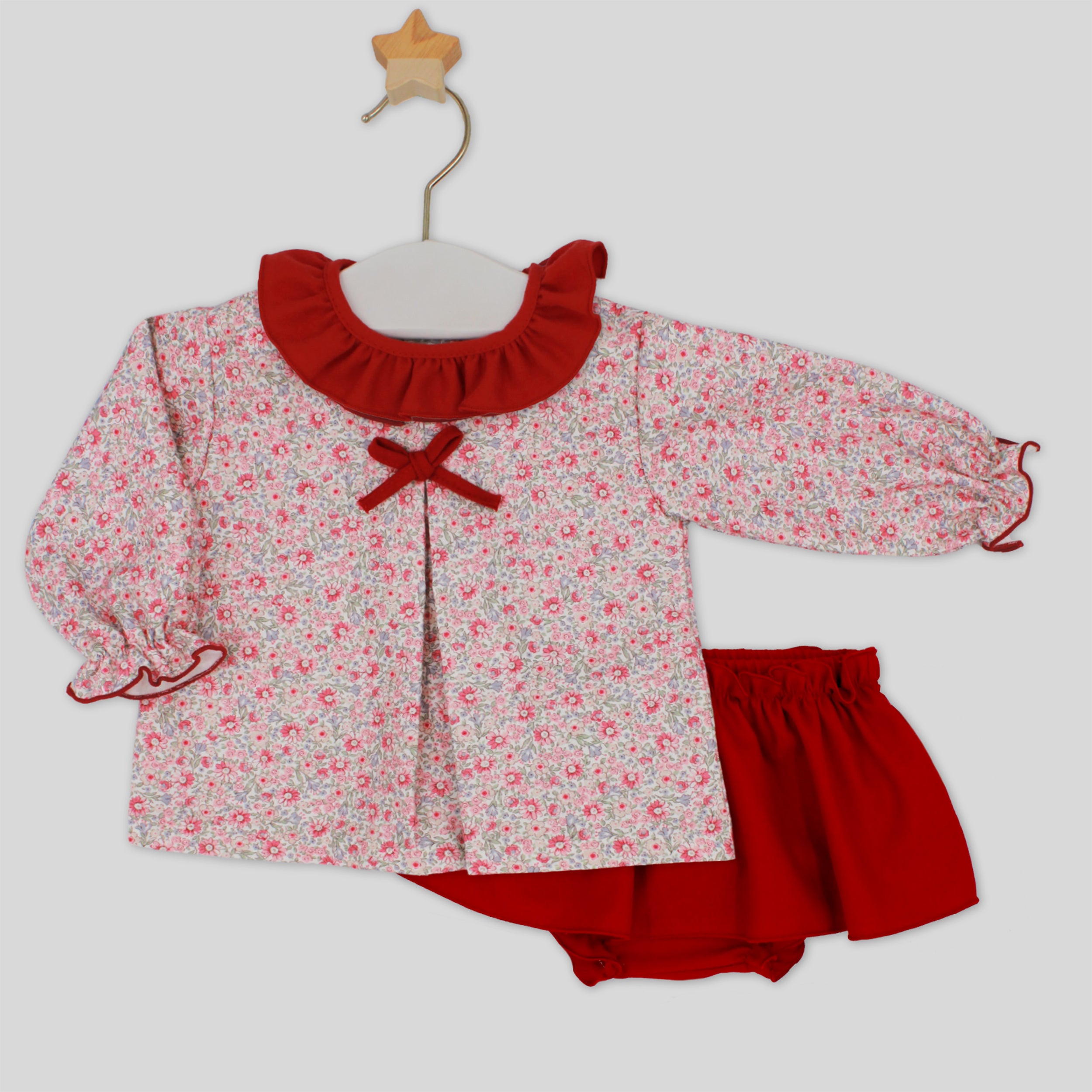 Children's outfit with floral top and red shorts on a hanger against a white background