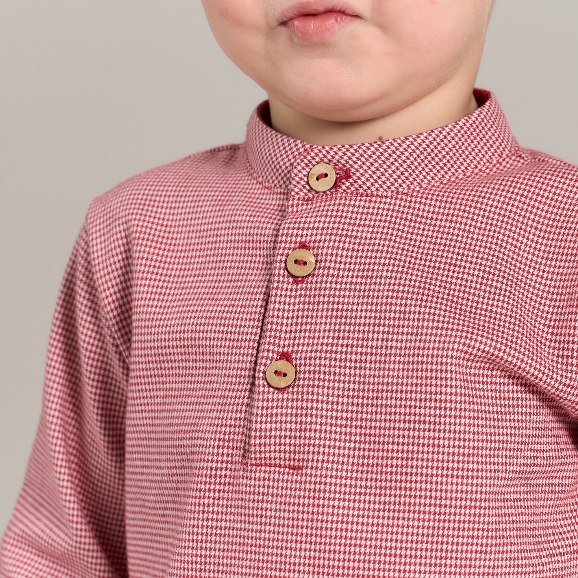 Child wearing a red checkered shirt with wooden buttons on a gray background