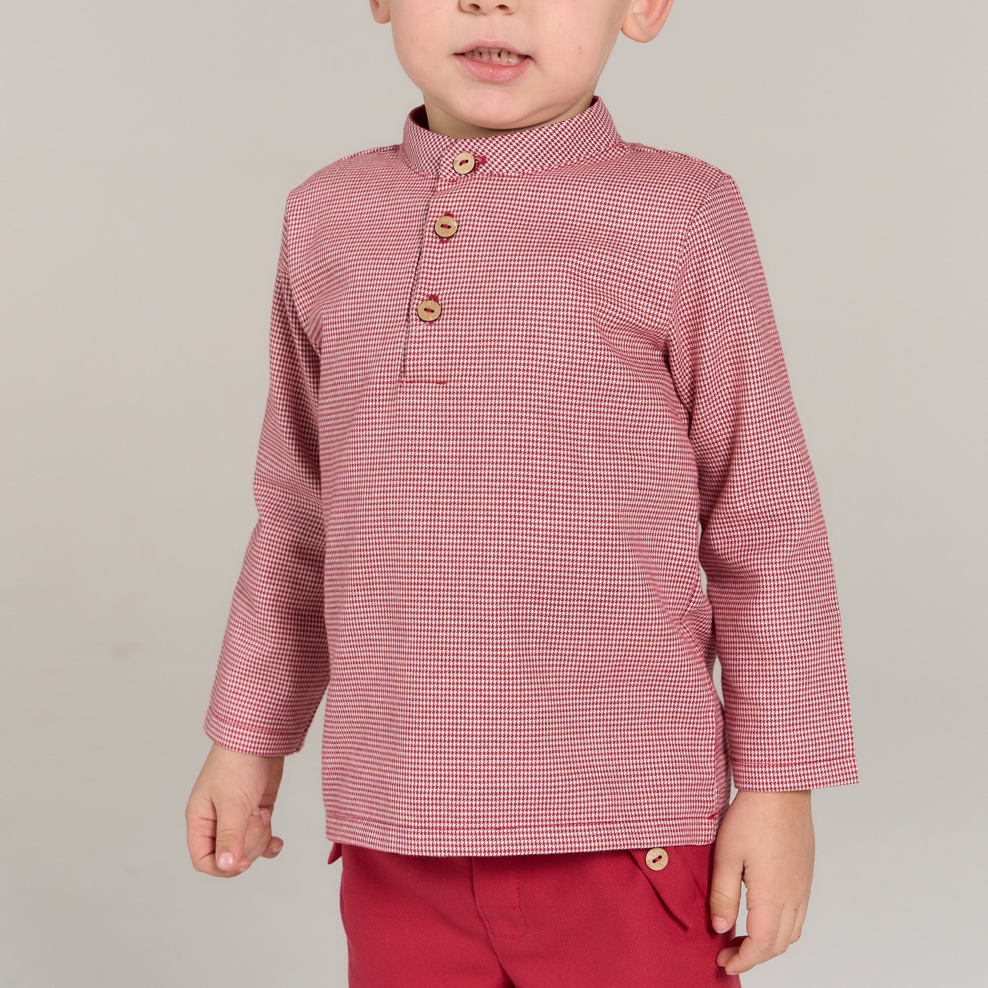 Child wearing a red checkered shirt and pants on a gray background