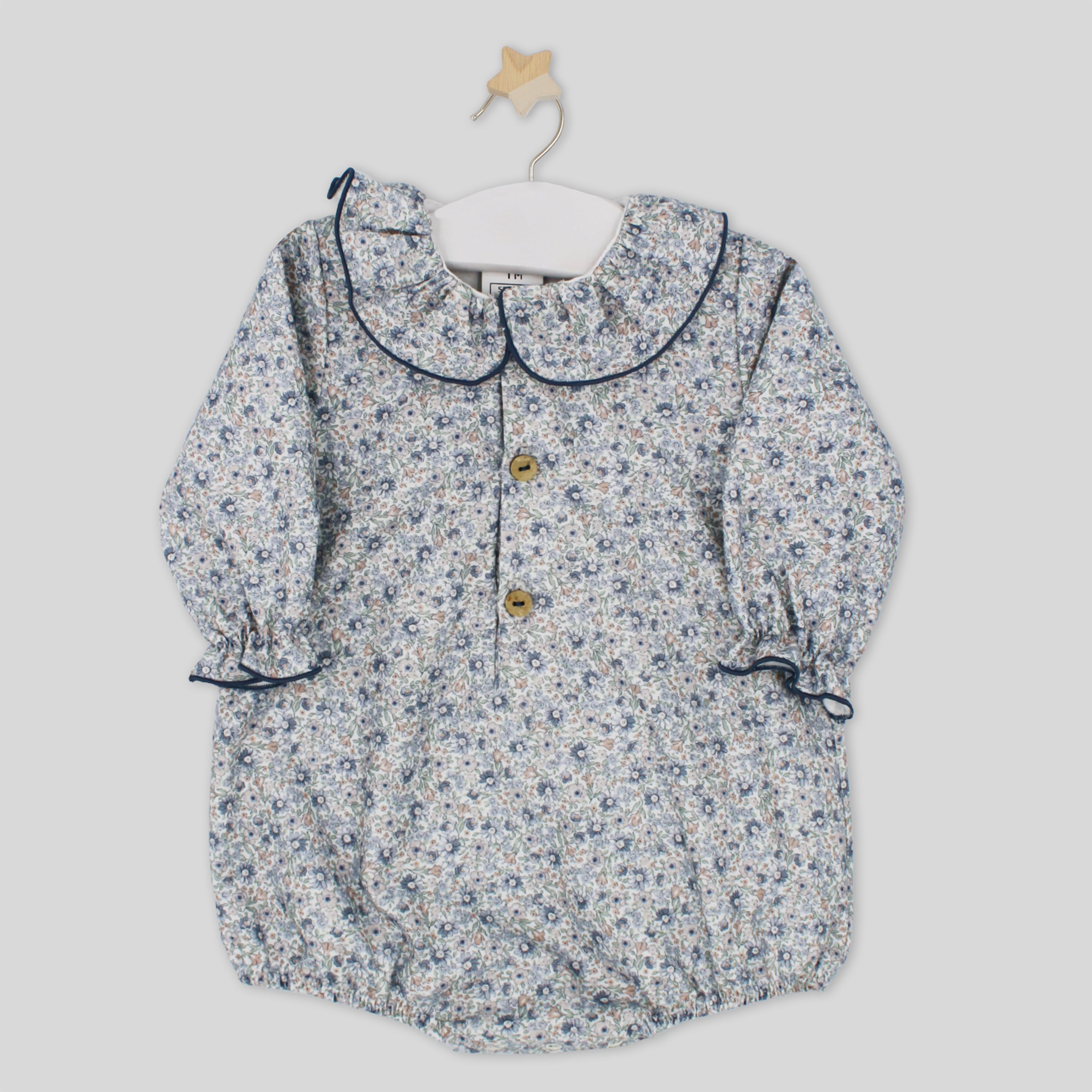 Floral patterned baby dress on a hanger against a light gray background