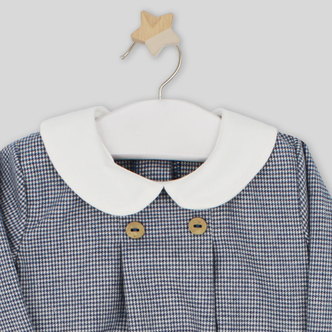 Children's dress with white collar and wooden buttons on a hanger against a light gray background