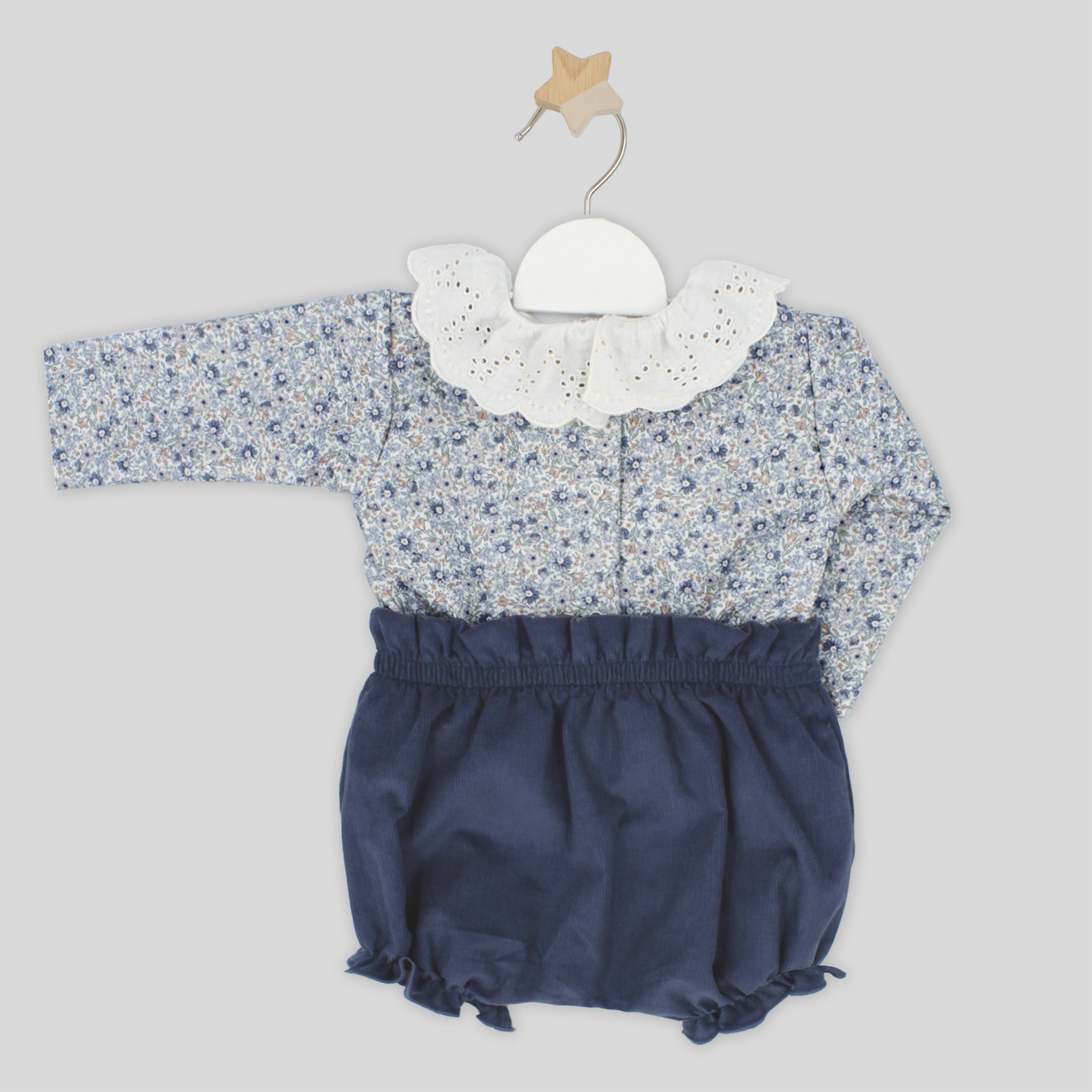 Baby outfit with floral top and navy bloomers on a hanger against a light gray background