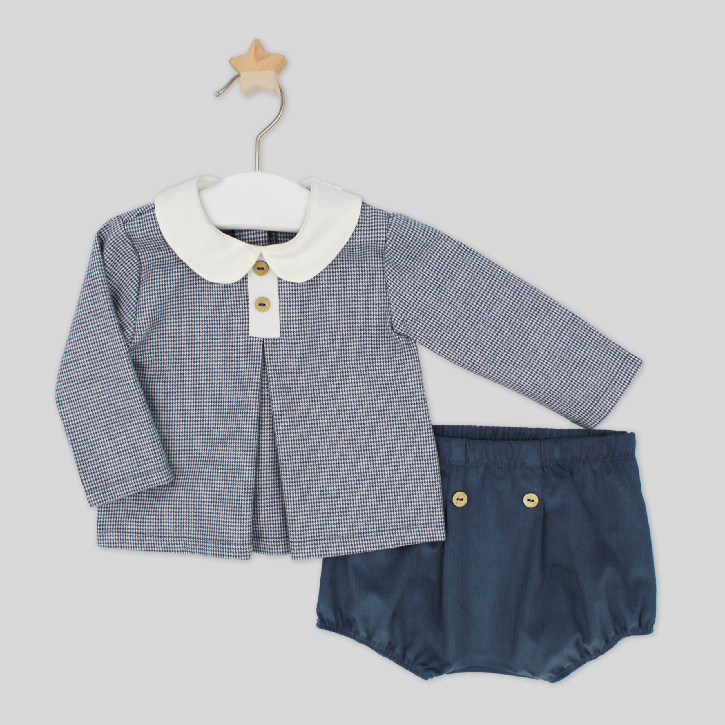 Baby outfit with checkered shirt and navy bloomers on a hanger against a light gray background