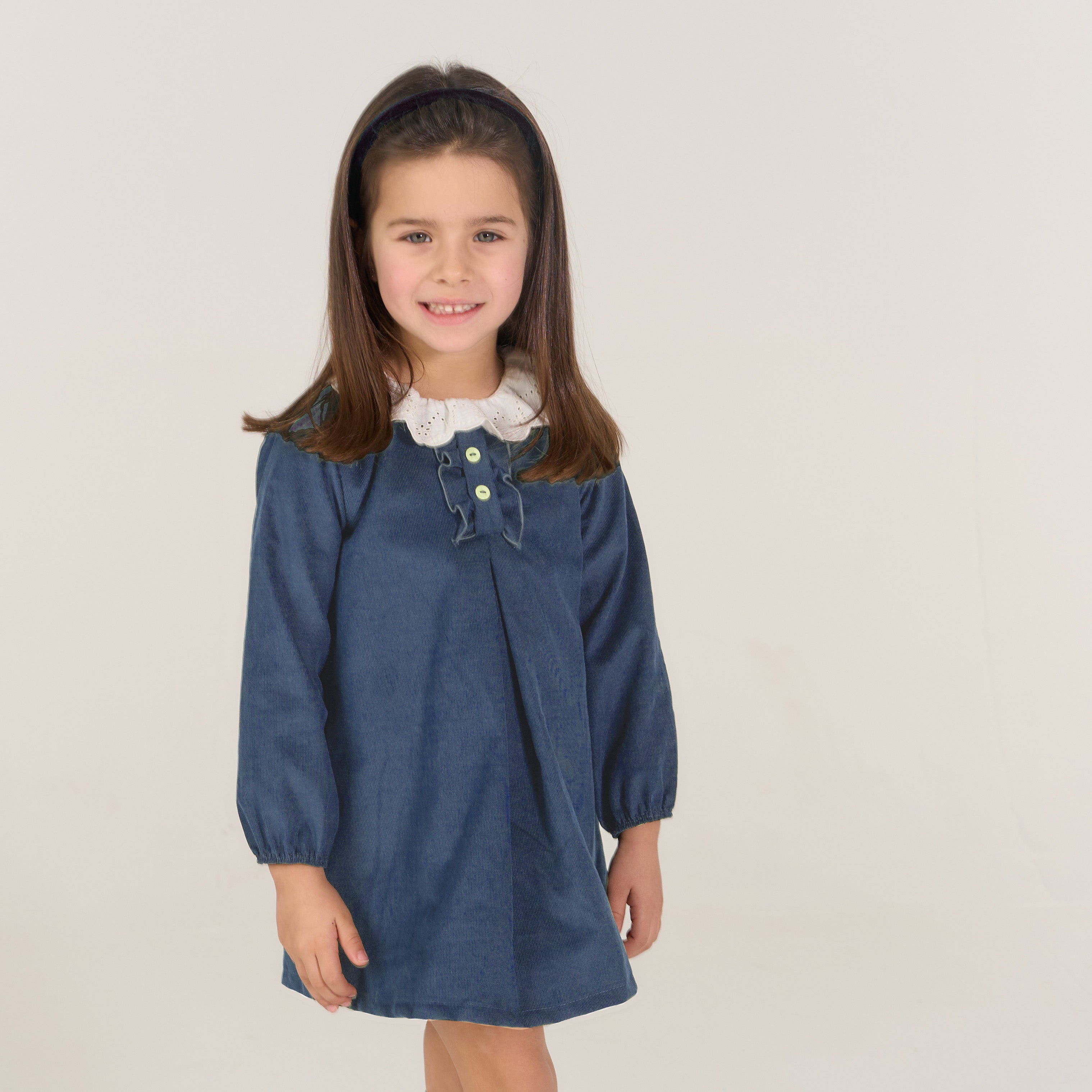 Young girl wearing a blue dress with a white collar against a plain background