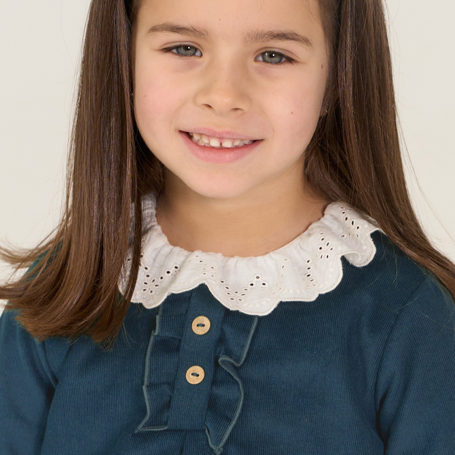 Young girl wearing a blue dress with a white lace collar against a plain background