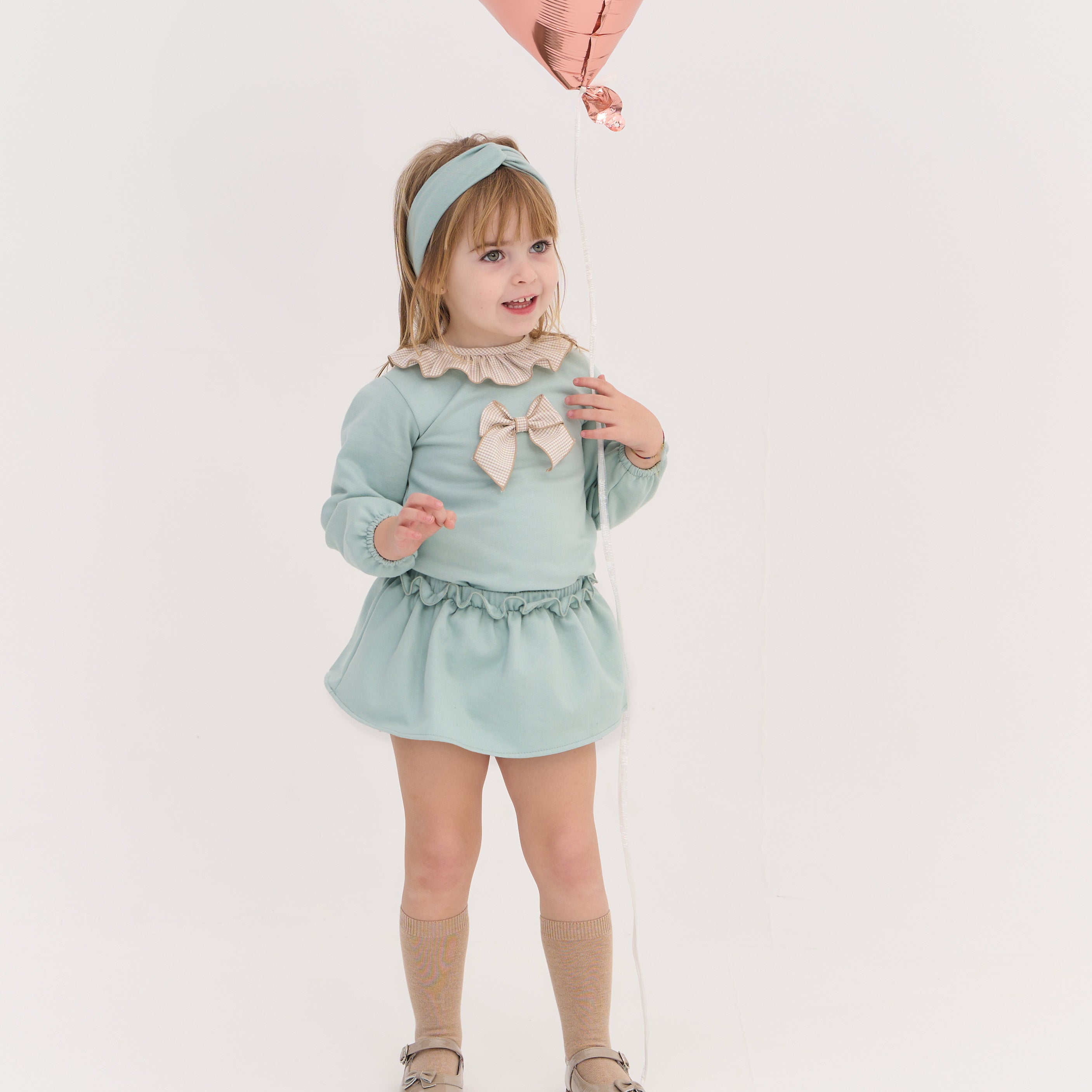 Young girl in a light blue dress with a bow holding a pink balloon against a white background