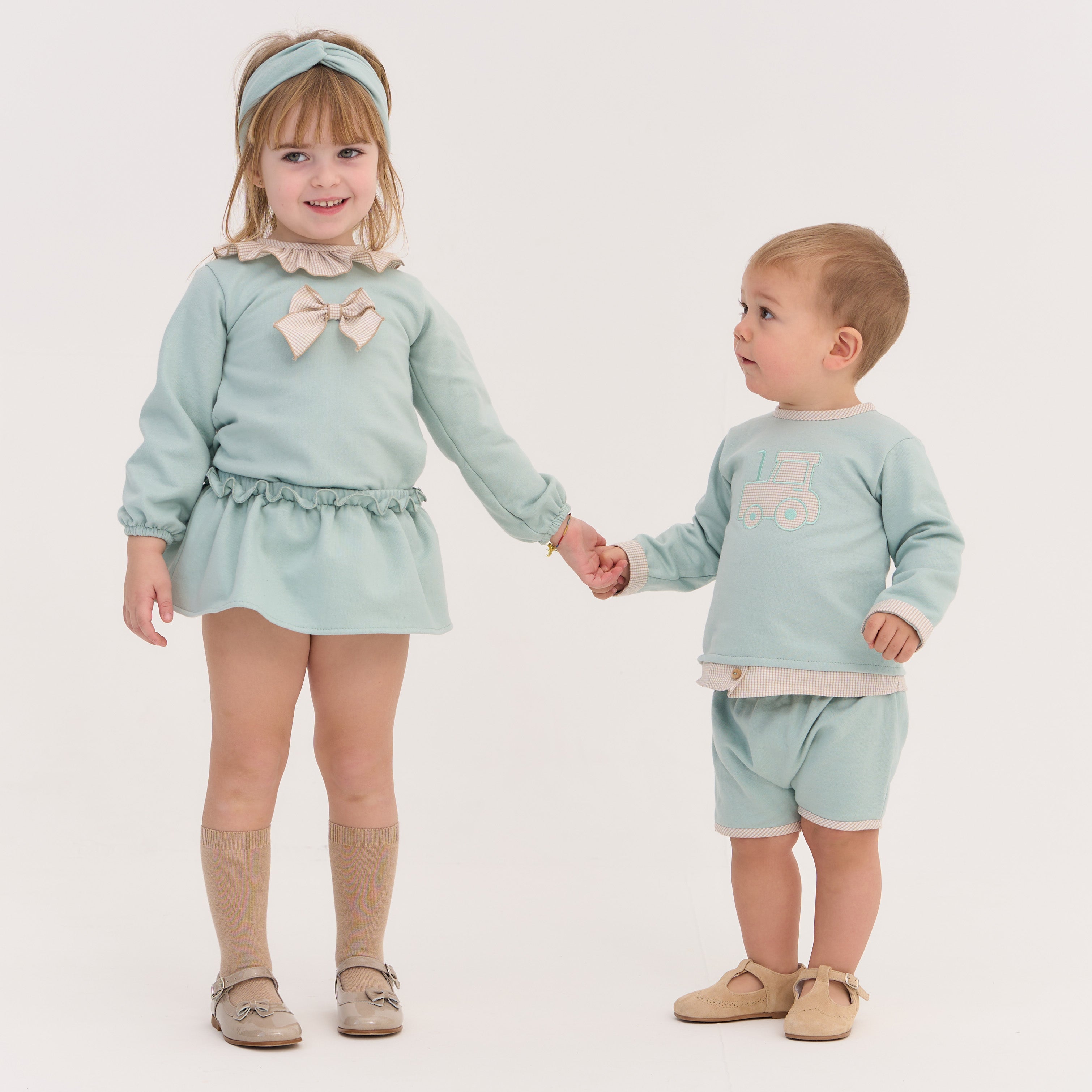 Two children holding hands, wearing matching light blue outfits on a white background