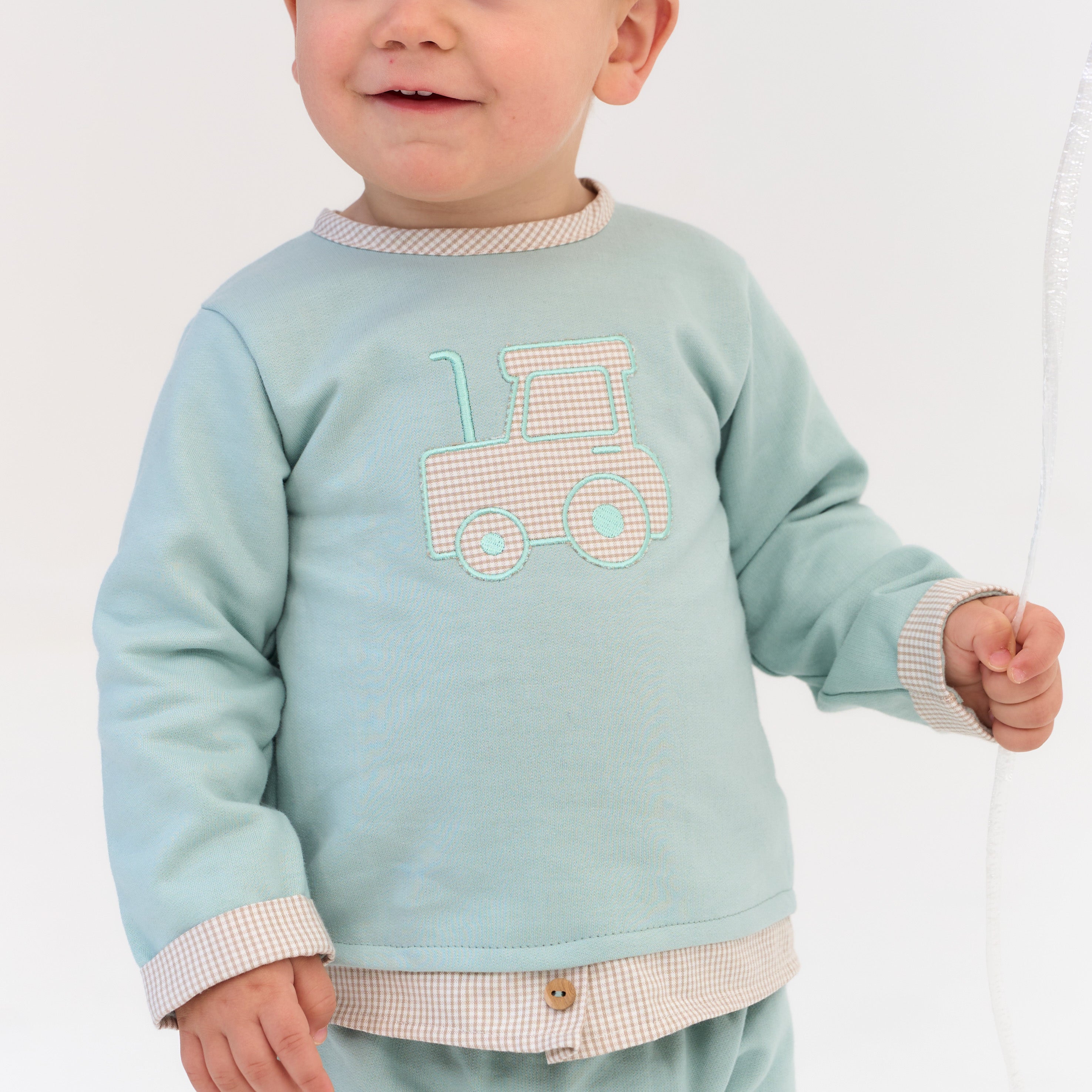 Child wearing a light blue sweatshirt with a tractor design on a plain background