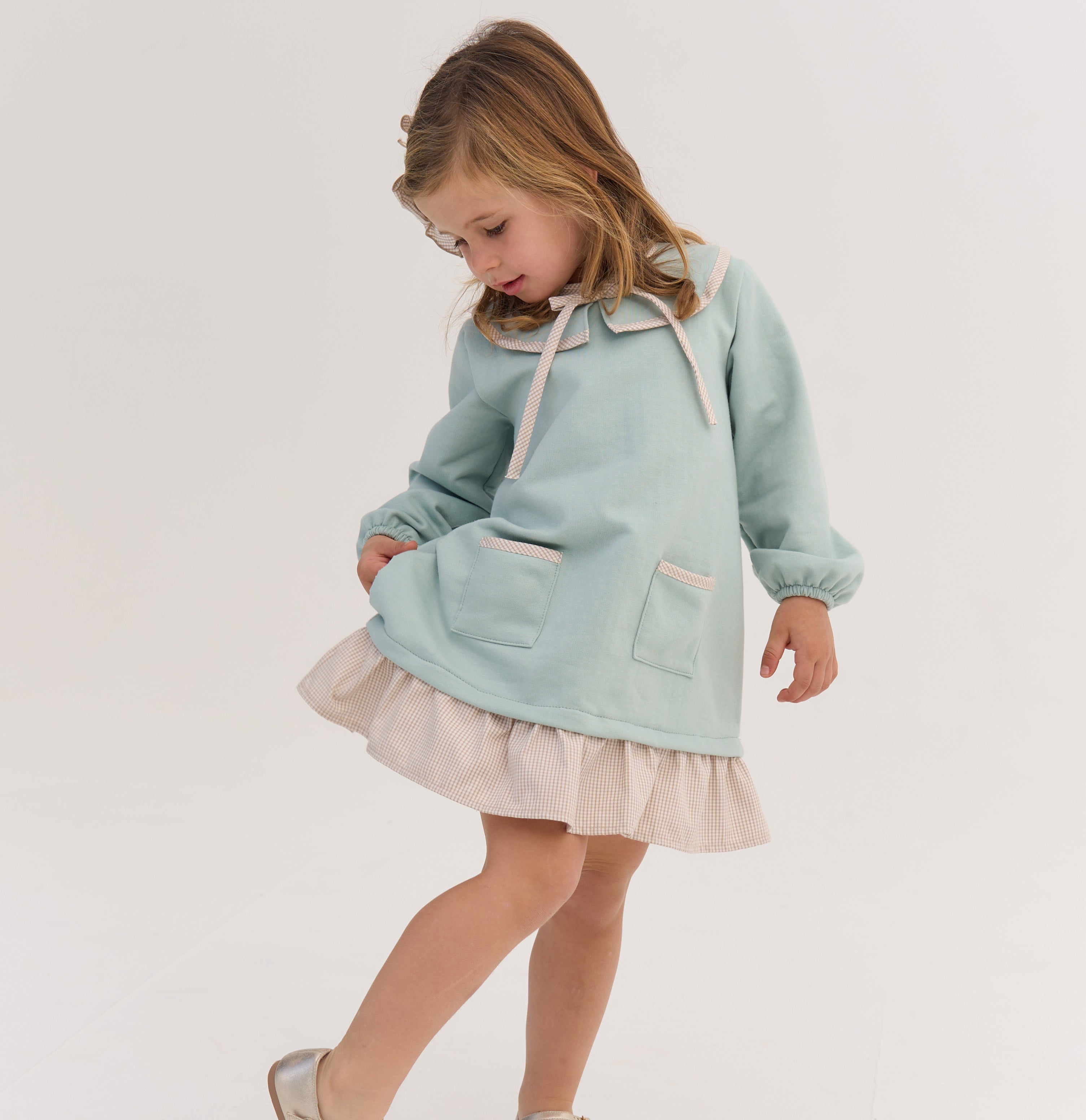 Young girl wearing a light blue dress with a white collar and skirt on a plain background