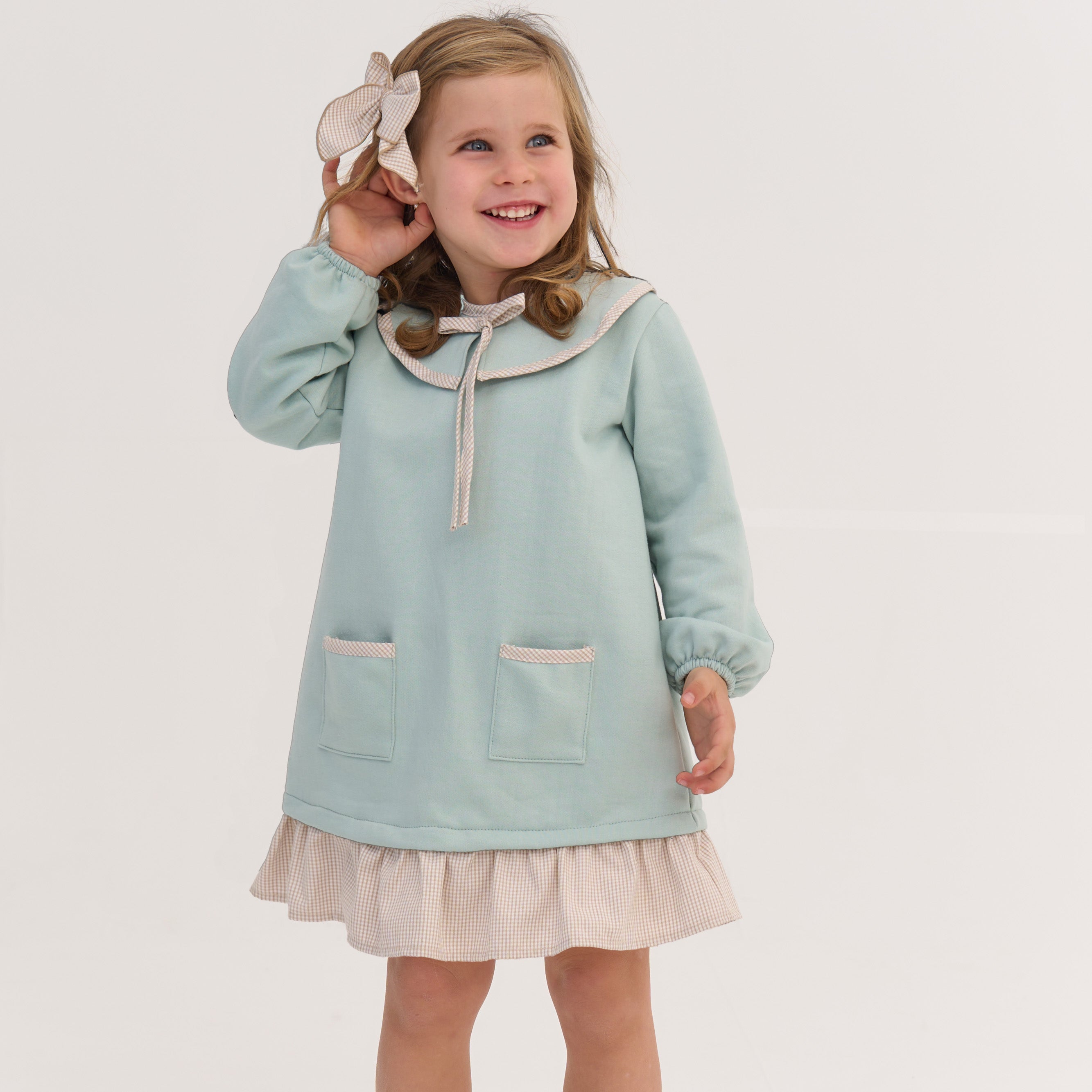 Young girl wearing a light blue dress with a white collar on a plain background