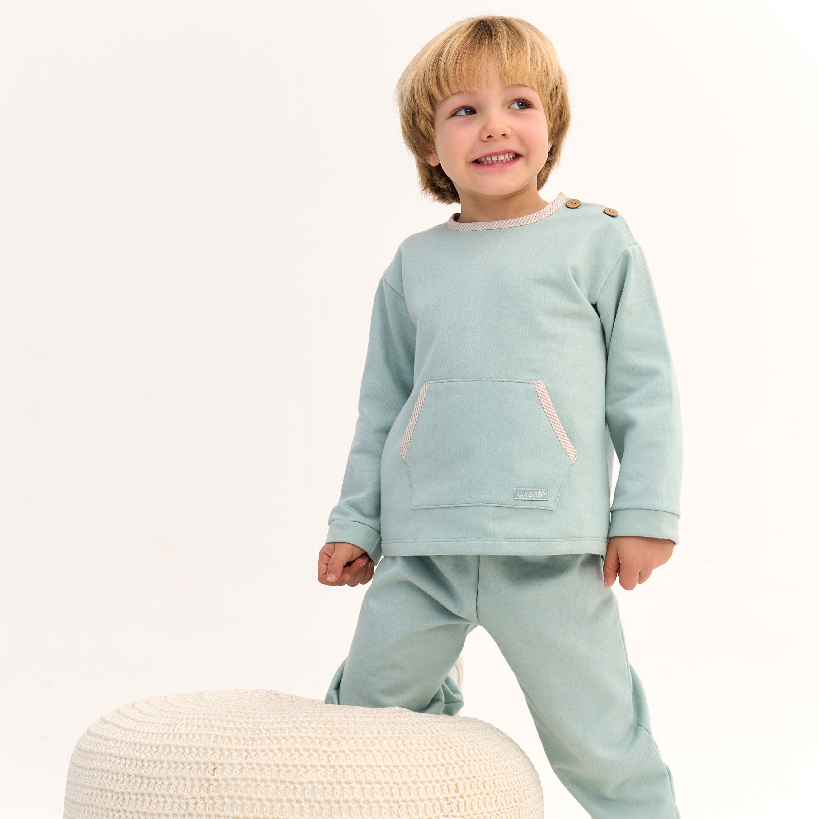 Child wearing a light blue outfit standing on a white background