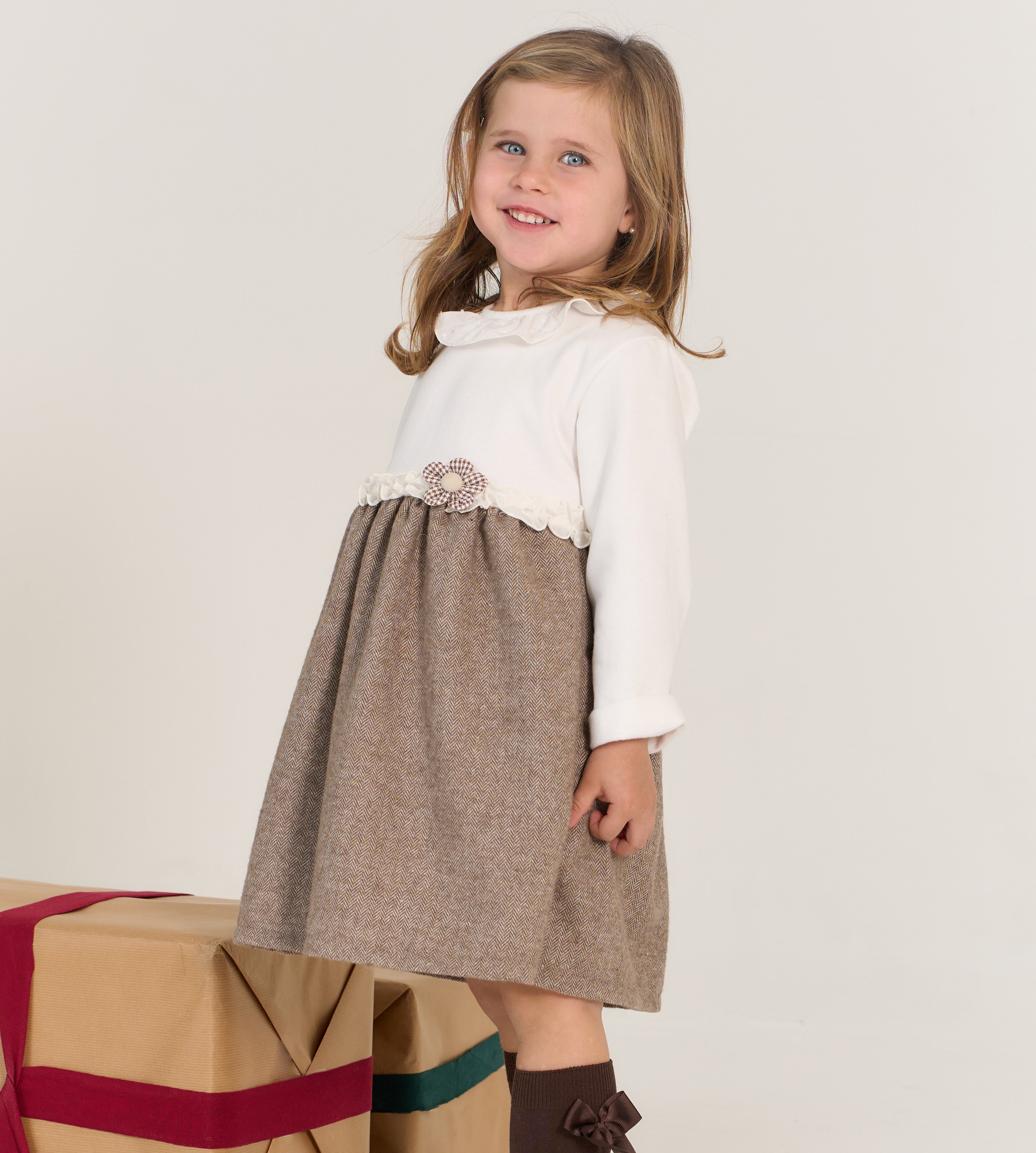 Young girl wearing a white blouse with lace details and a brown skirt on a plain background.