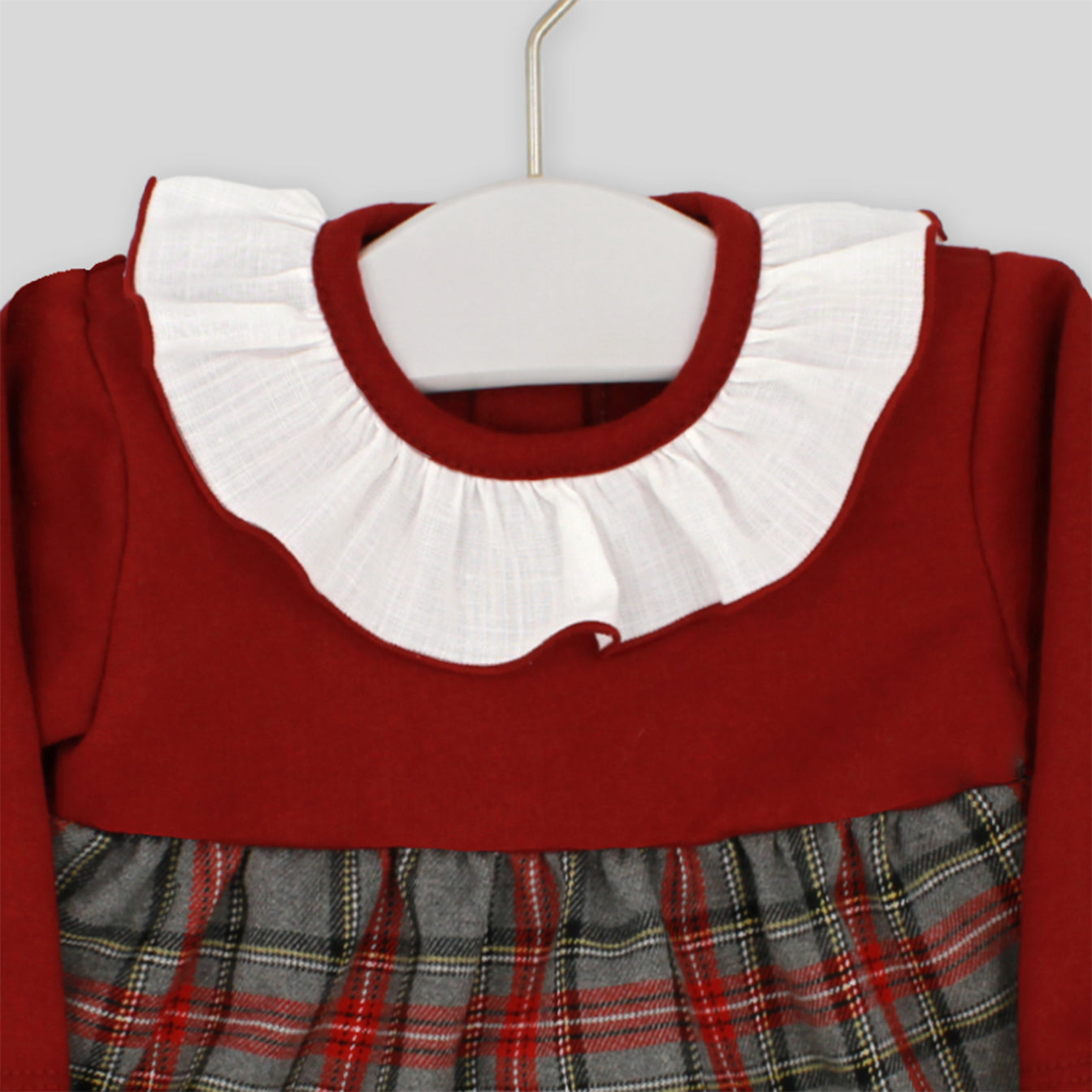 Red dress with white collar and plaid skirt on a hanger against a gray background