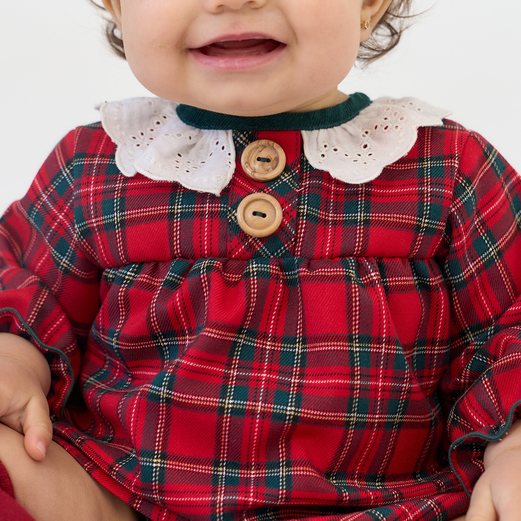 Child wearing a red plaid dress with white collar and buttons on a plain background