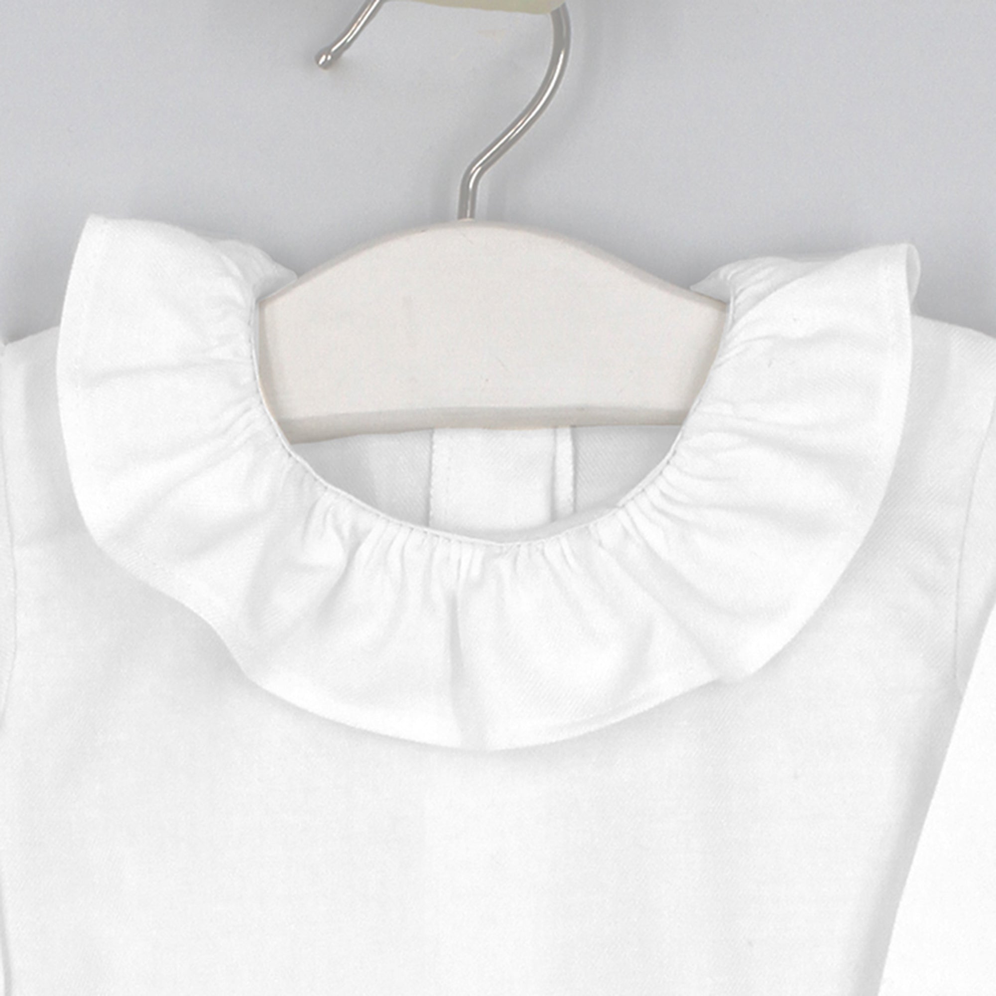 White blouse with a ruffled collar on a hanger against a light gray background