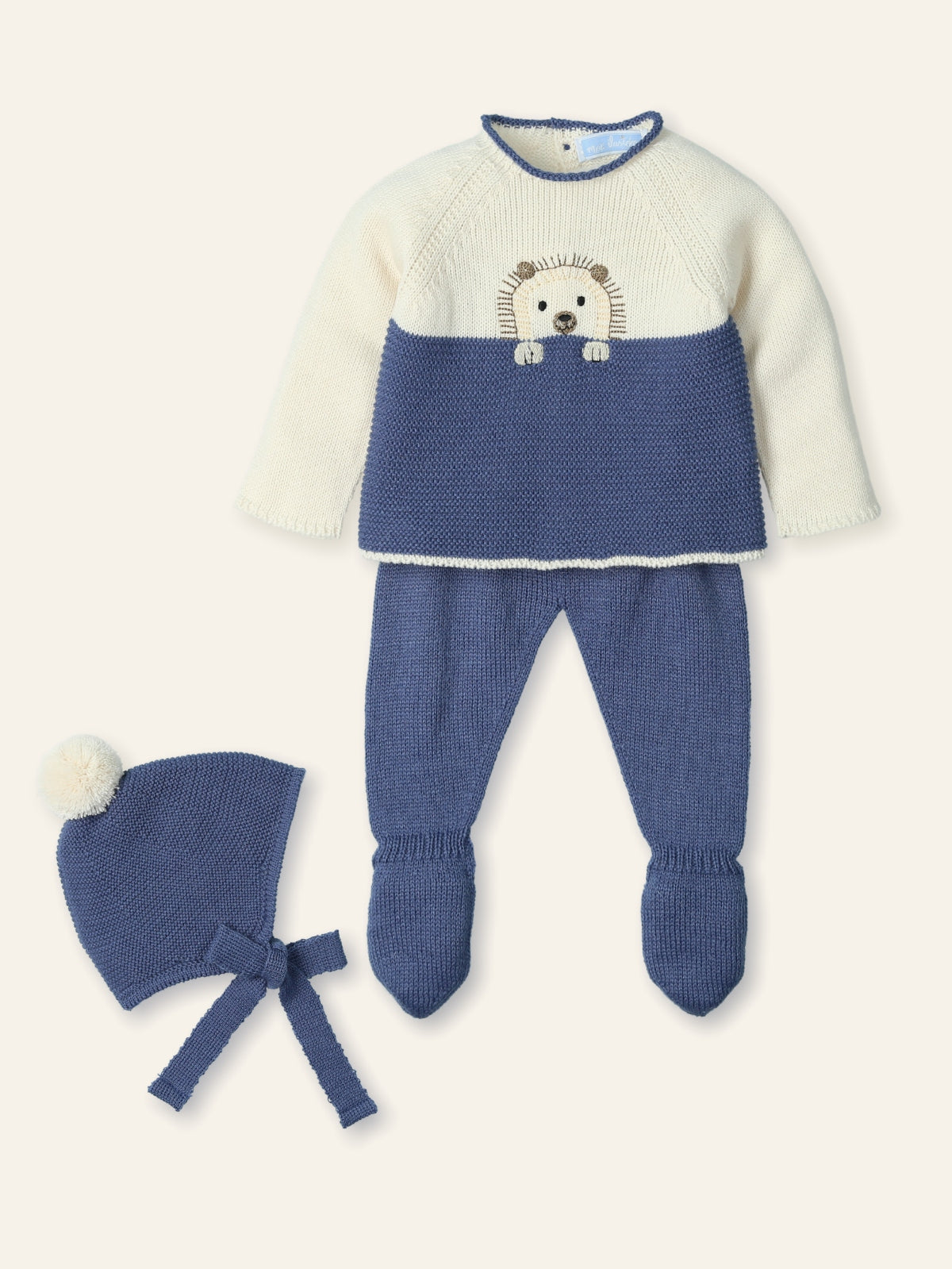 Baby outfit with blue knitted pants and hat, and cream sweater with bear design on a white background.