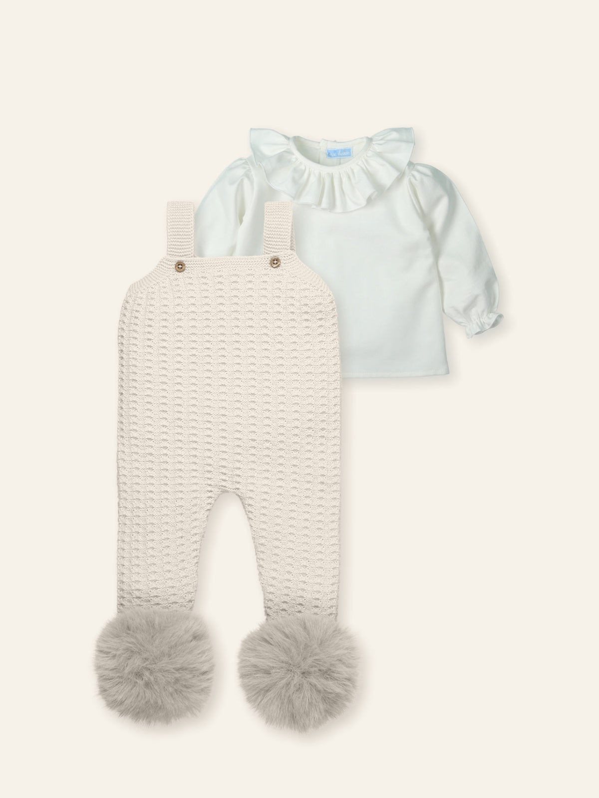 Baby outfit with light blue top and white knitted romper with pom-poms on a white background