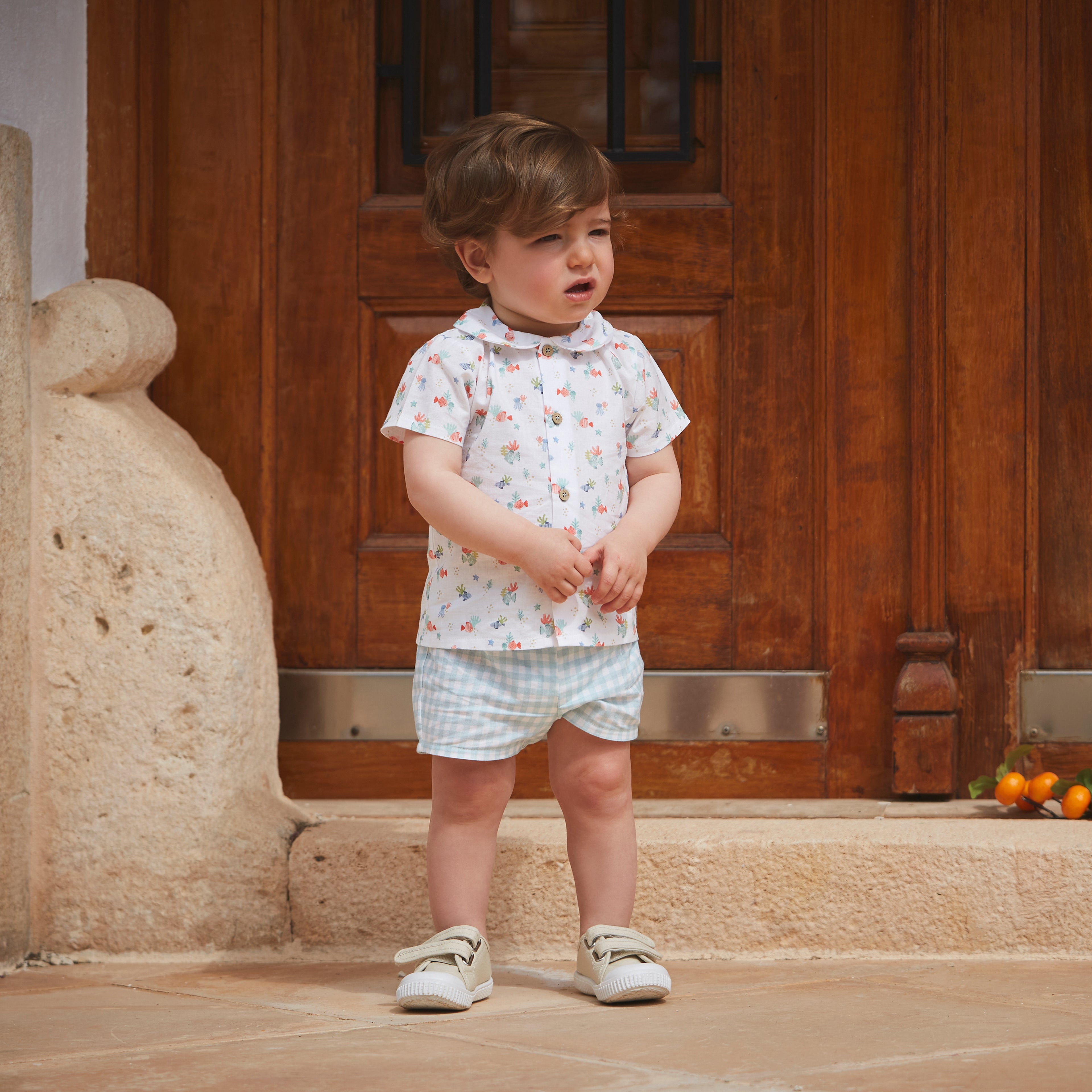 Child standing in a room with wooden doors and stone wall.